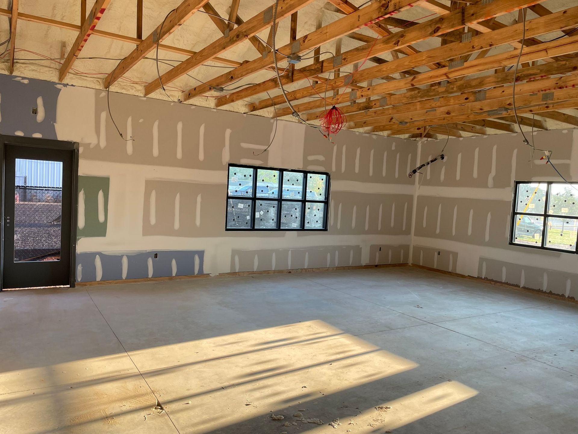 Interior construction site: unfinished walls, exposed beams, concrete floor, door, windows.