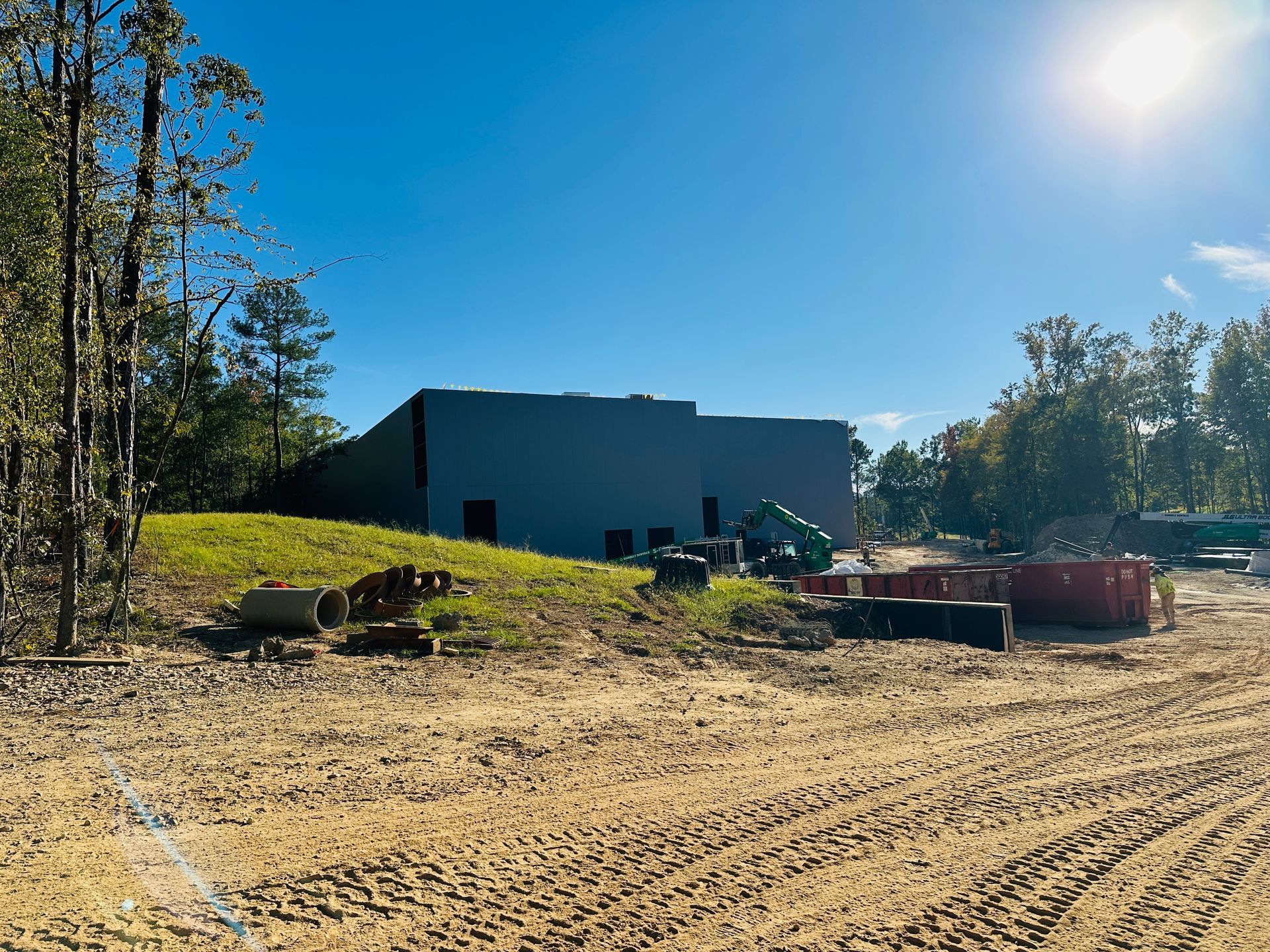 Construction site with a large blue building, dirt lot, and equipment under a bright sunny sky