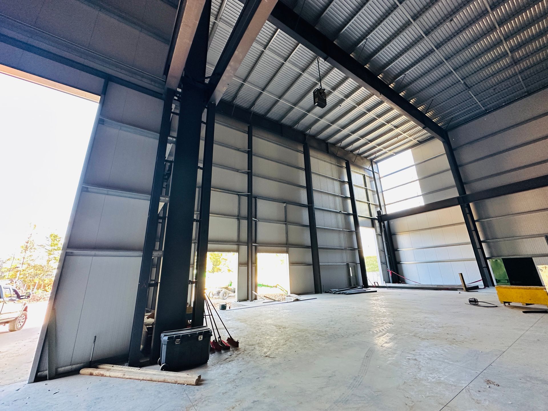 Empty industrial warehouse interior with metal walls, high ceiling, and open roll-up doors.