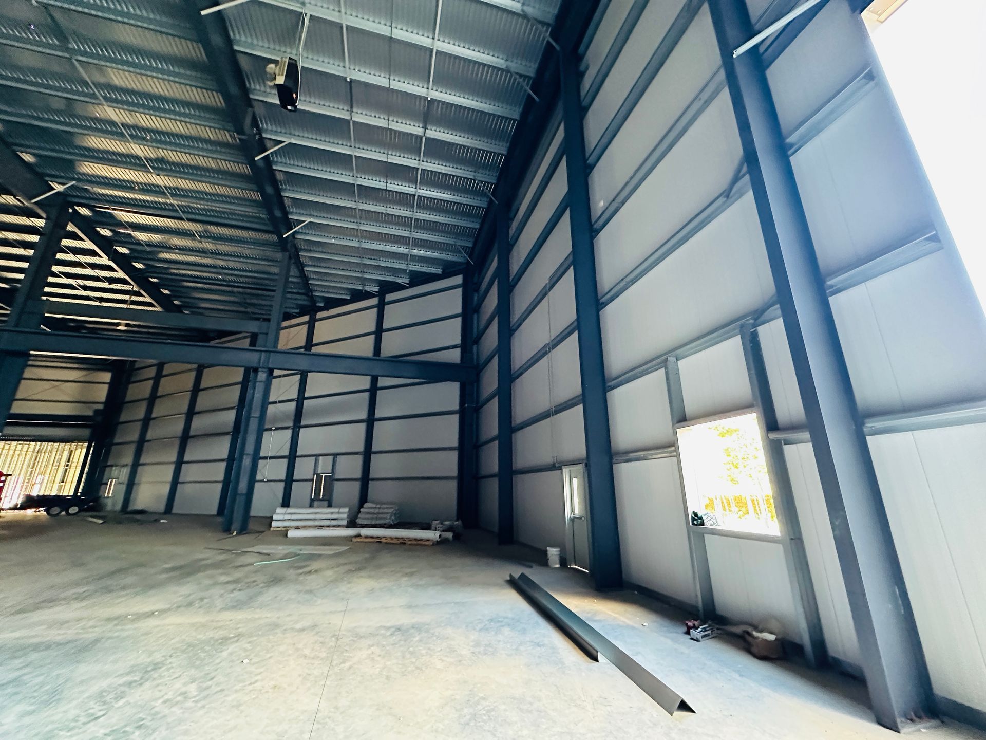 Empty steel-frame warehouse interior with high ceiling, concrete floor, and large open windows.