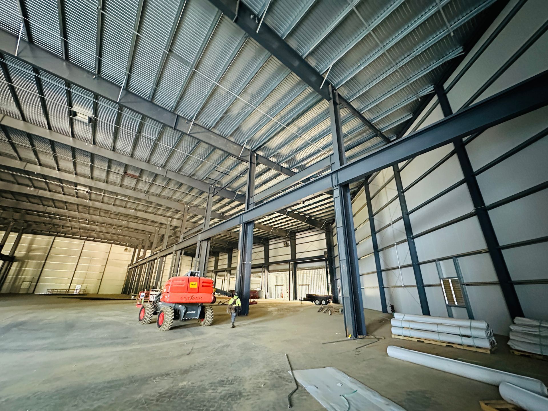 Interior of a warehouse under construction with steel framing, workers, and a red lift truck