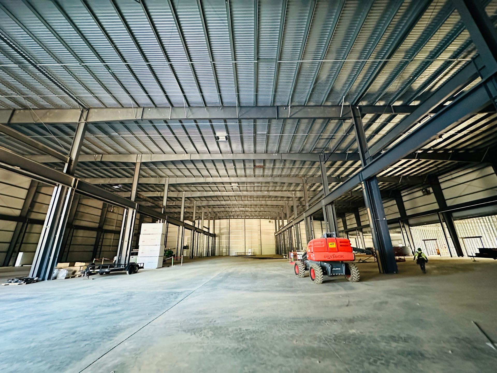 Empty steel-framed warehouse interior with a red scissor lift on the concrete floor