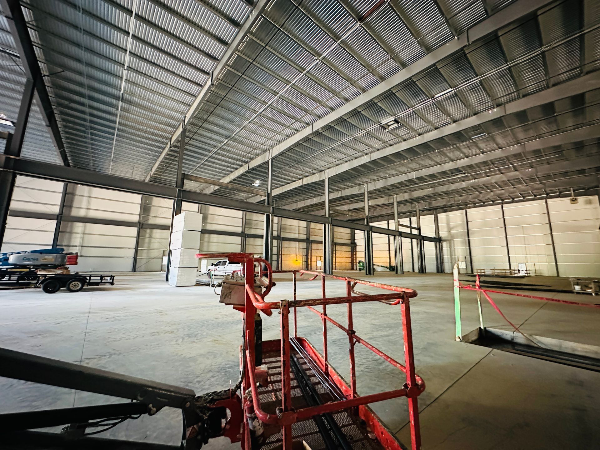 Empty industrial warehouse interior with steel beams, red lift platform, and a truck near the wall.