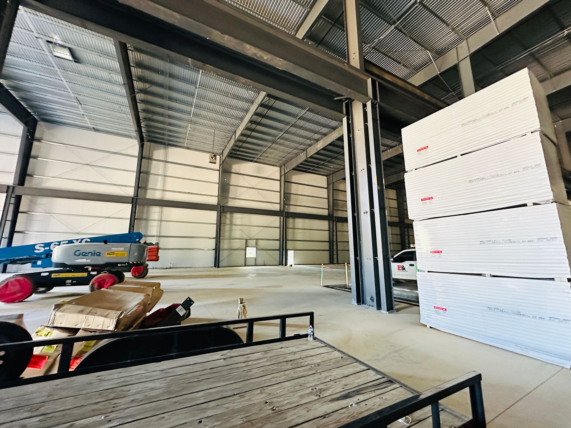Industrial warehouse interior with stacked white insulation panels and a blue scissor lift