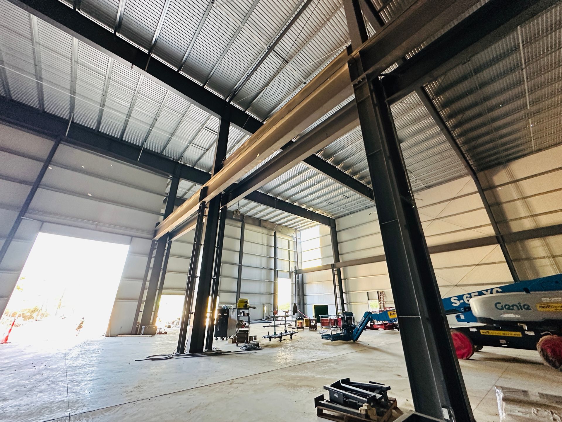 Large warehouse interior with steel beams, open bay doors, and construction equipment inside