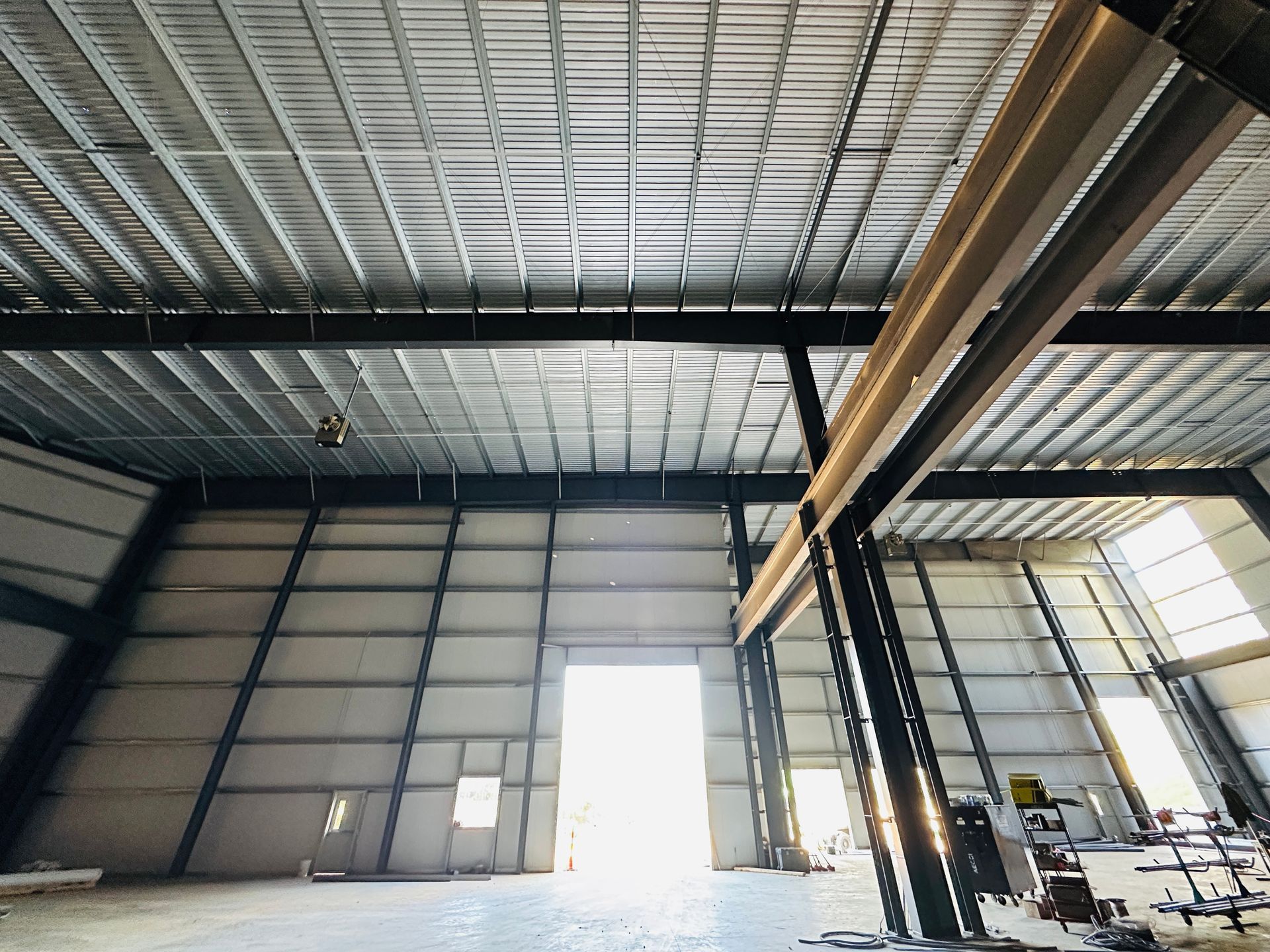 Large empty warehouse interior with steel beams, high ceiling, and a bright open loading door