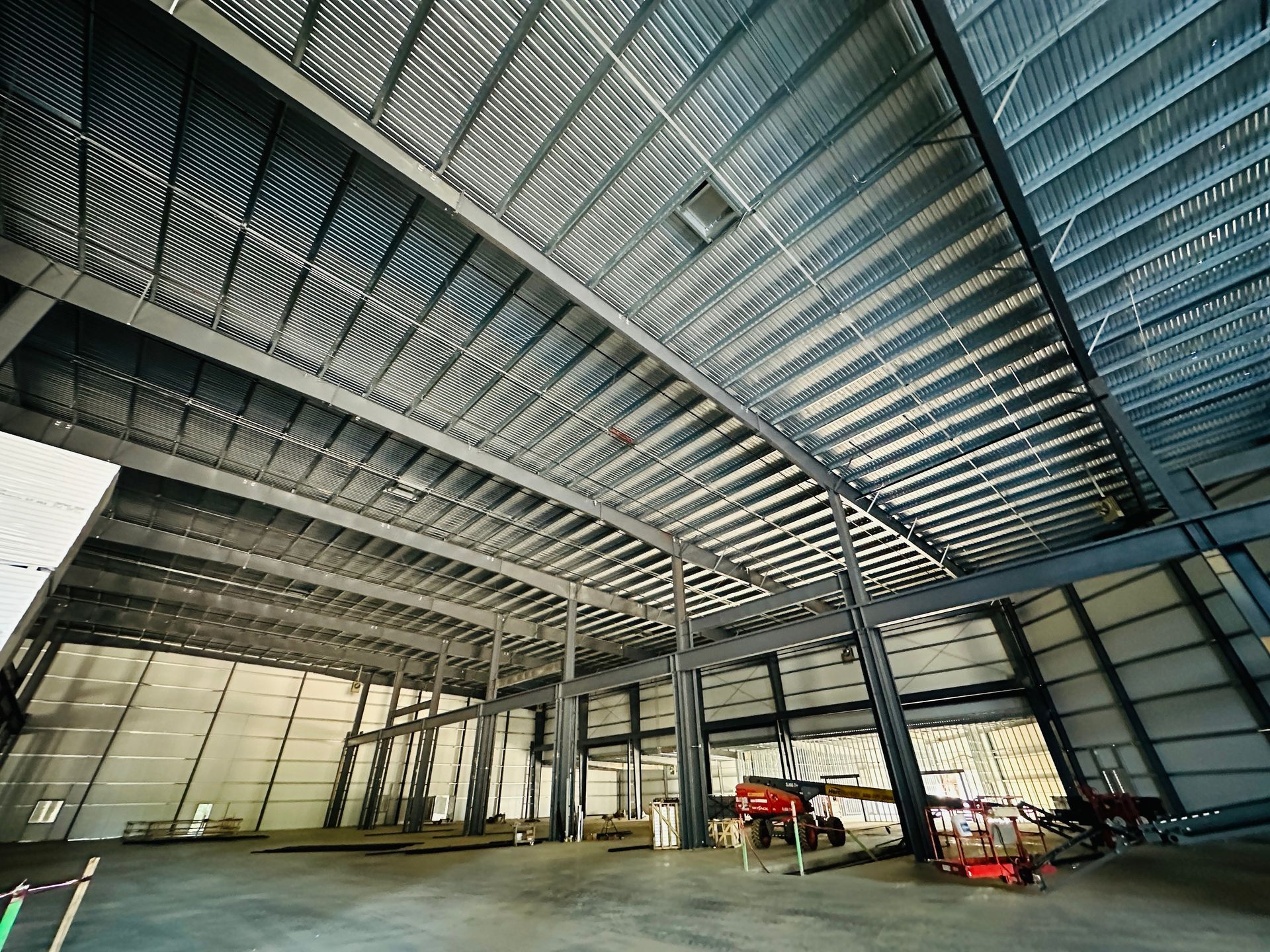 Large industrial warehouse interior with exposed steel beams, high ceiling, and a few vehicles near the back.