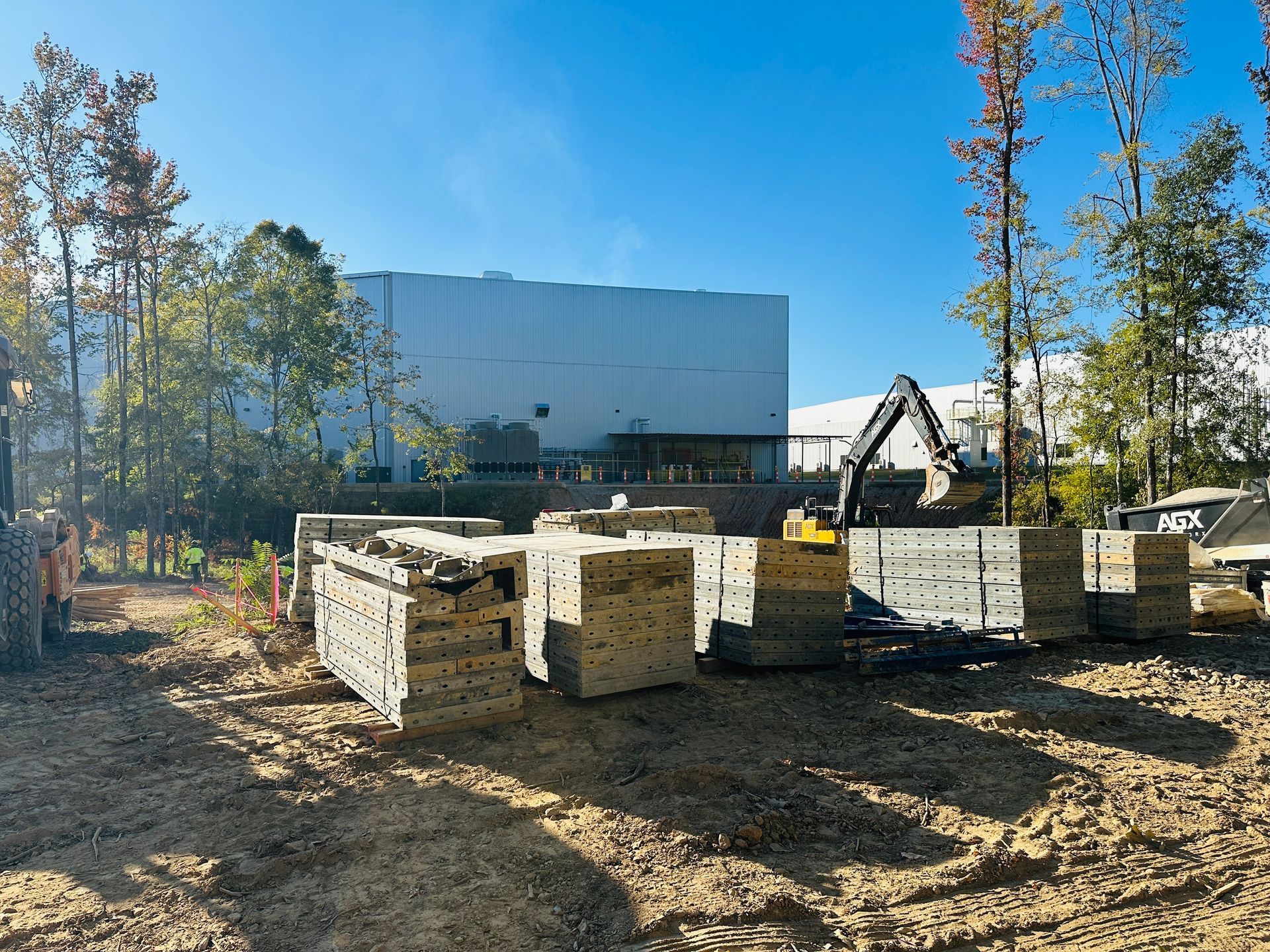 Stacks of lumber at a construction site with a large building and excavator in the background