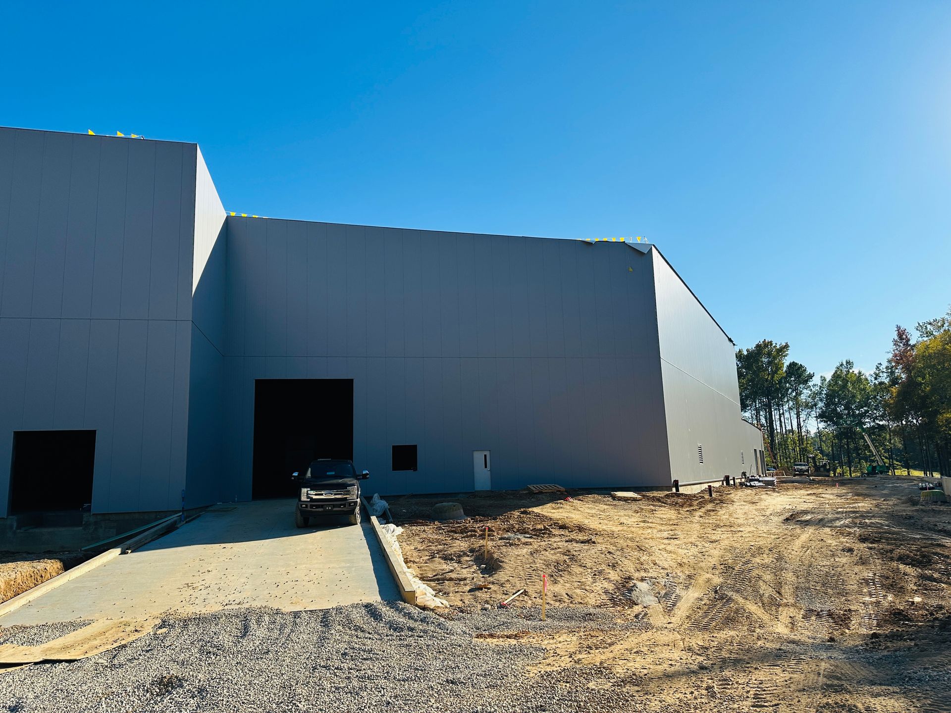Large gray industrial warehouse with an open loading bay and a dirt lot under a clear blue sky