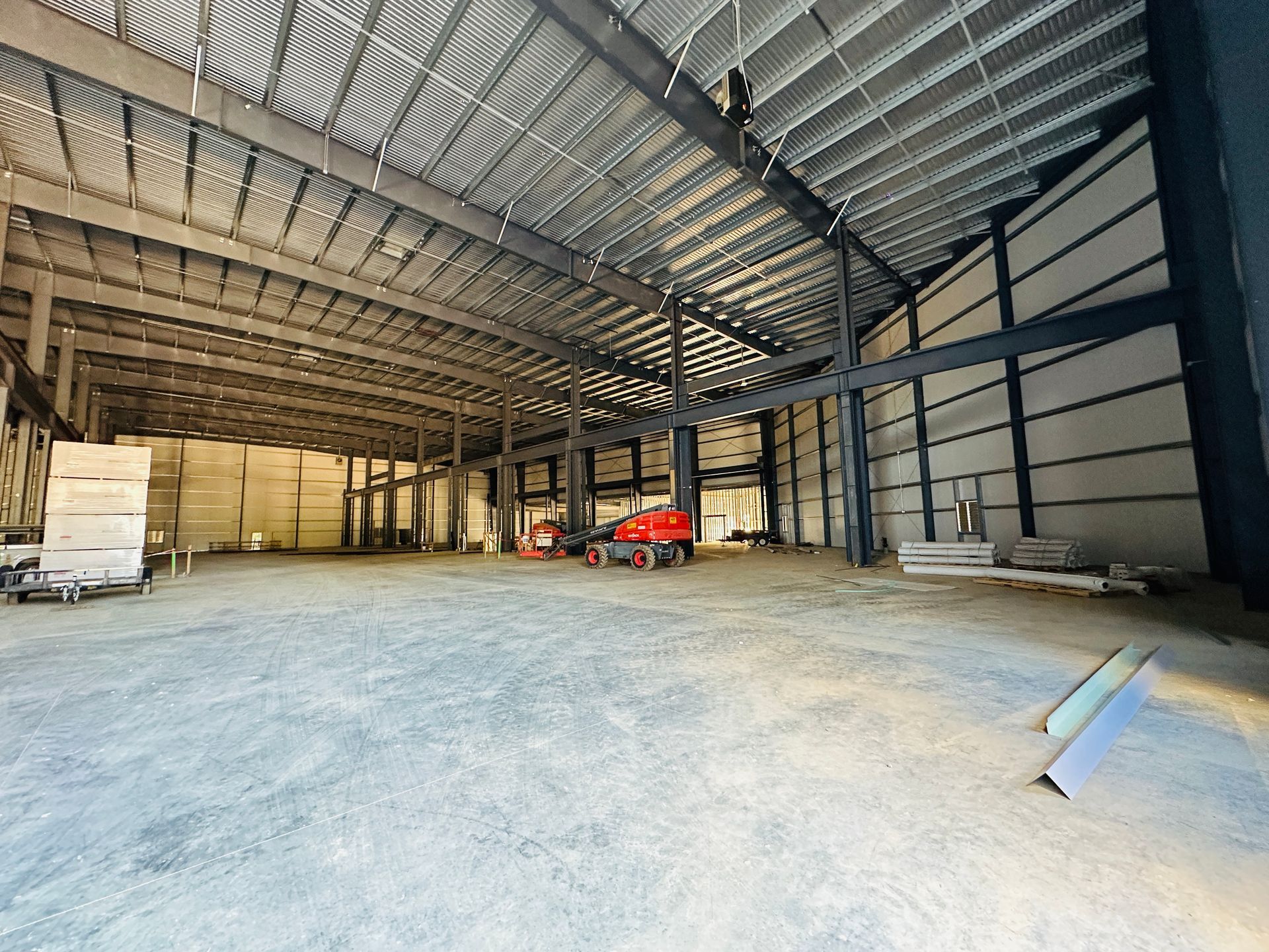 Empty warehouse interior with steel frame, concrete floor, and construction materials inside