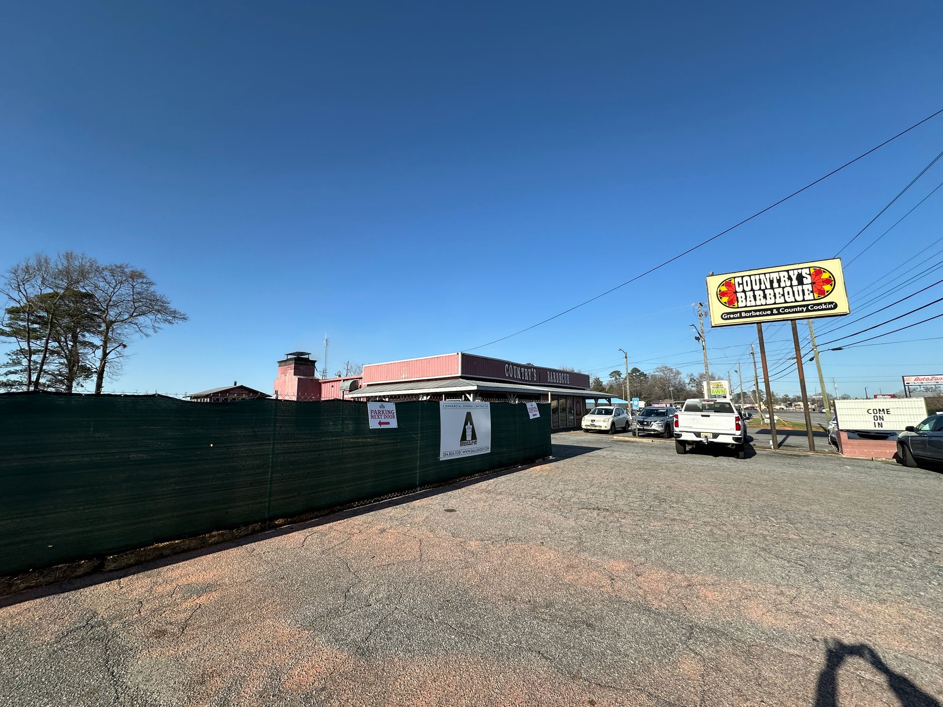 A parking lot with cars parked in front of a building and a billboard.