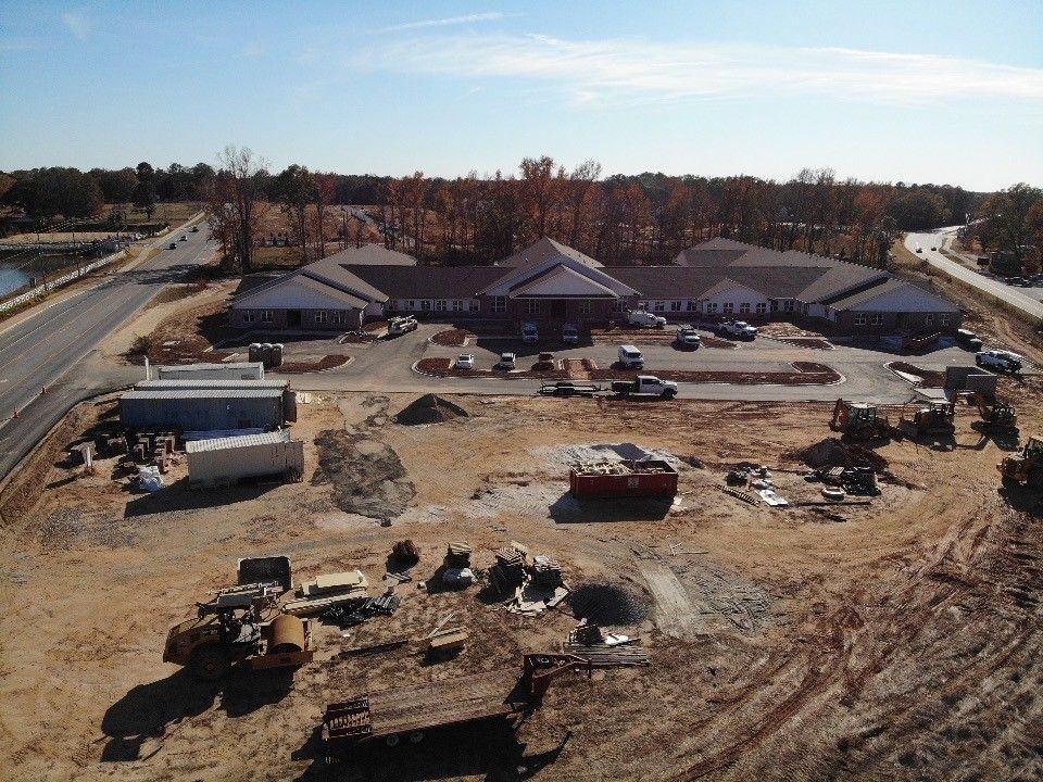Construction site with a partially built, multi-wing building; dirt, machinery, and containers.