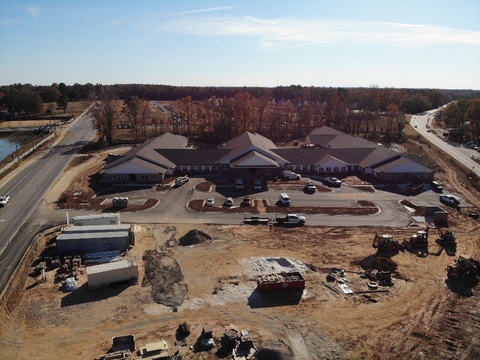 Aerial view of a long, brown-roofed building under construction; vehicles and equipment dot the dirt site.