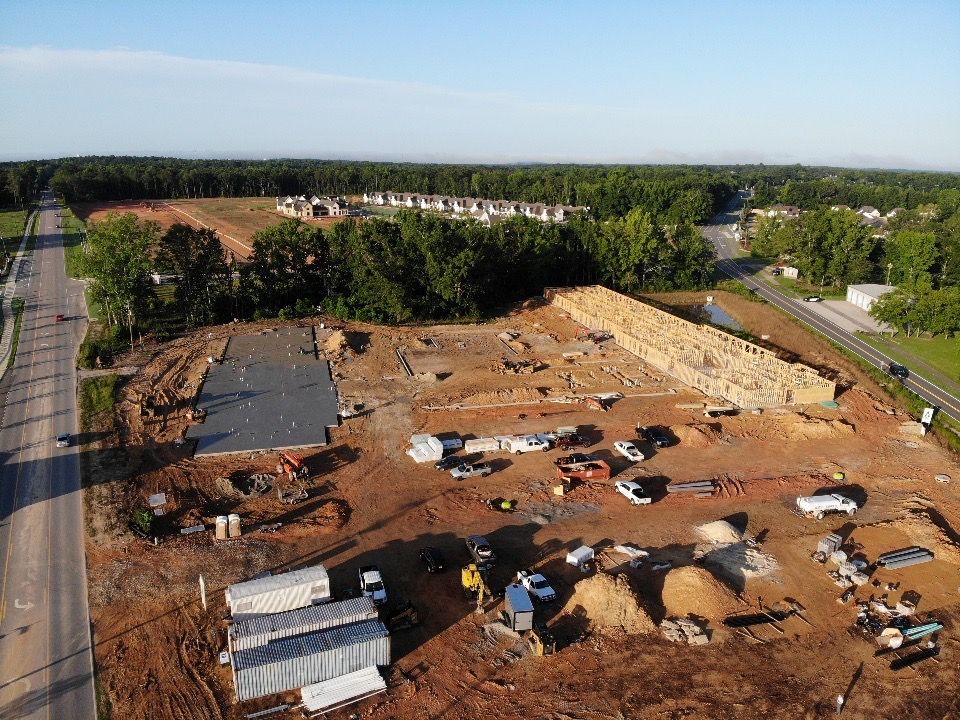 An aerial view of a construction site surrounded by trees and a road.