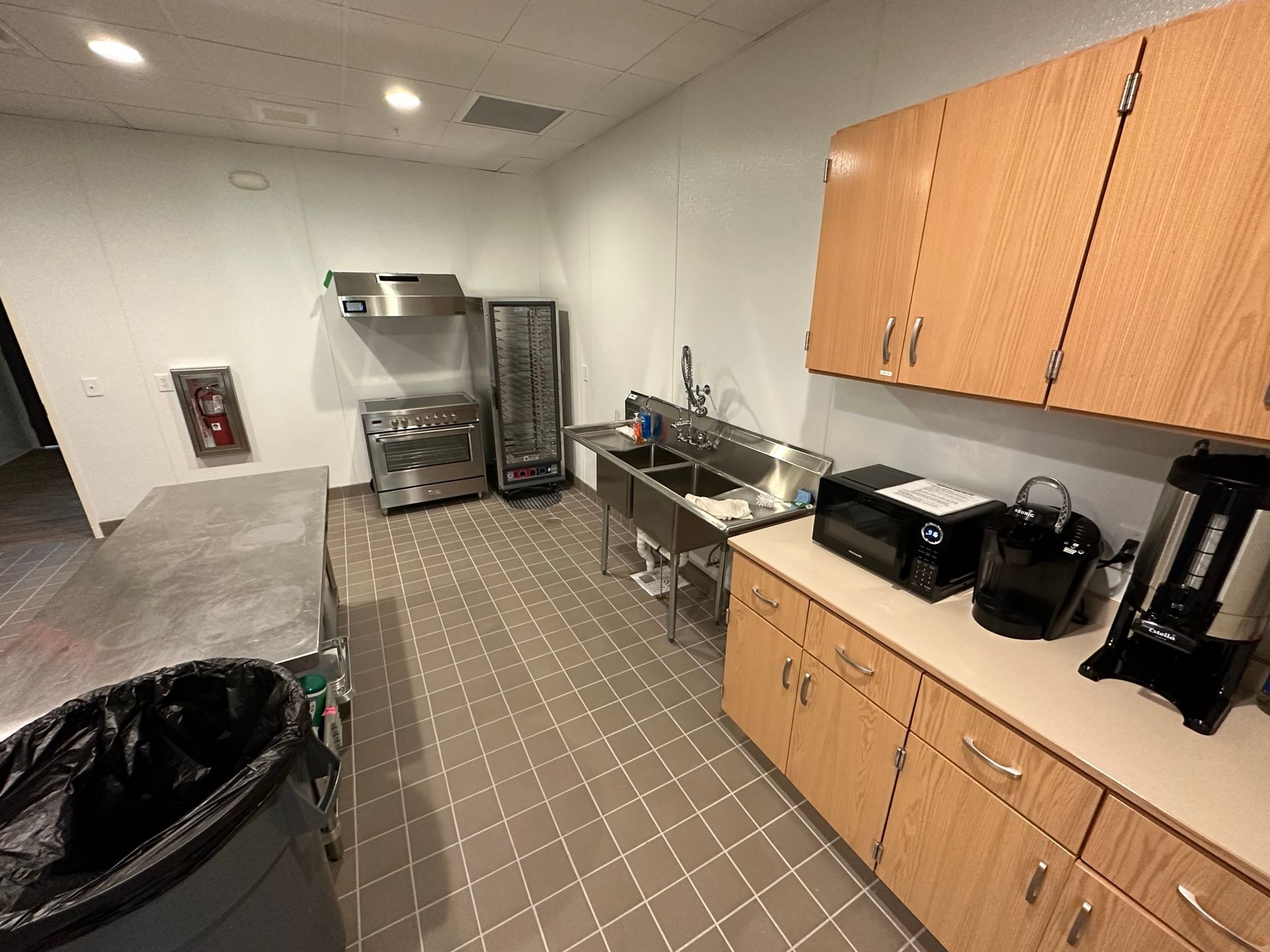 A kitchen with wooden cabinets , stainless steel appliances , a sink and a trash can.