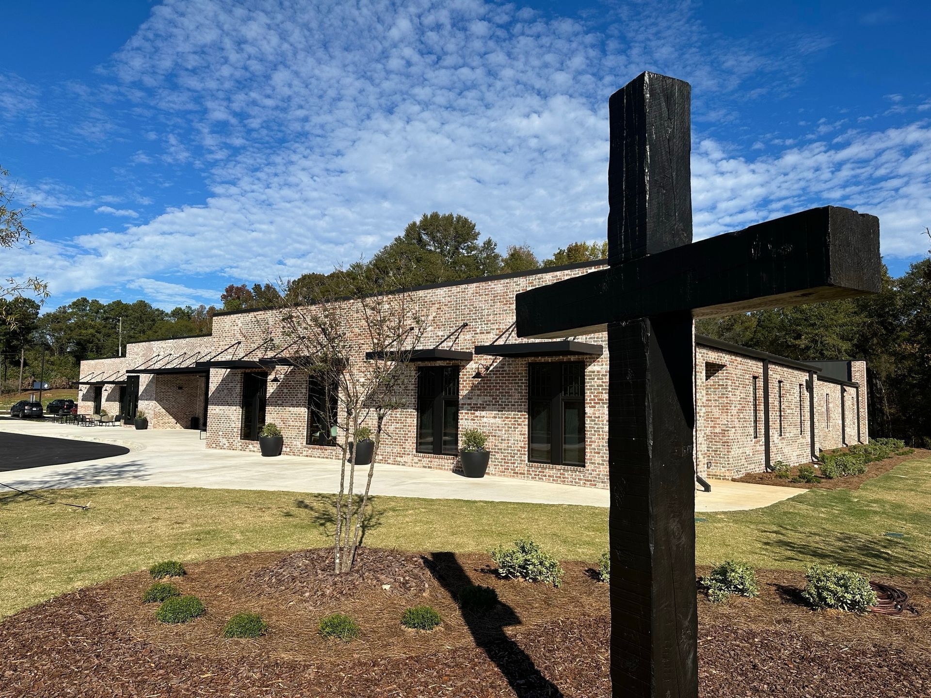 Stone church building with a large black cross sculpture in the foreground under a blue sky
