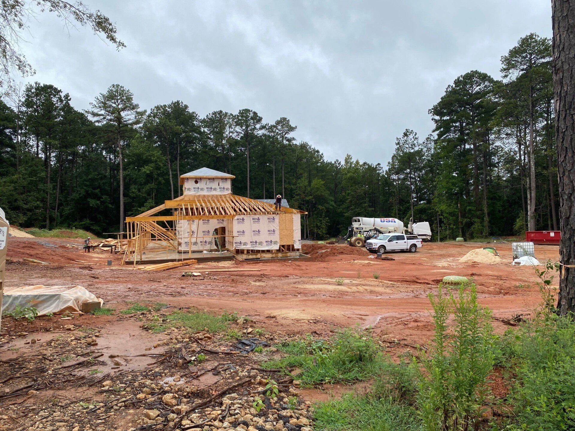 A house is being built in a dirt field with trees in the background.