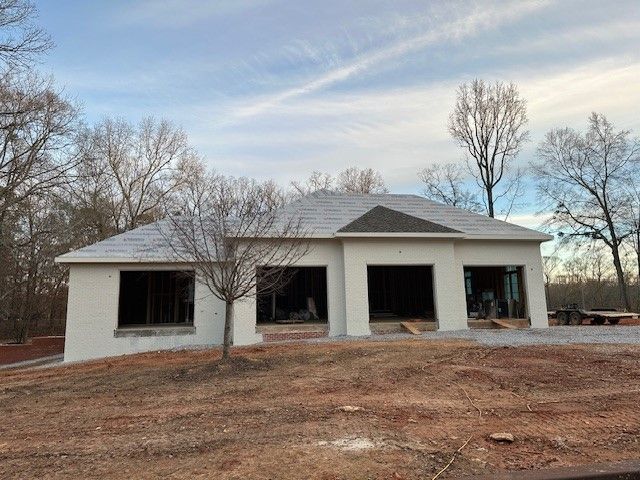 New house under construction, light stucco walls, dark roof, windows, and bare trees.
