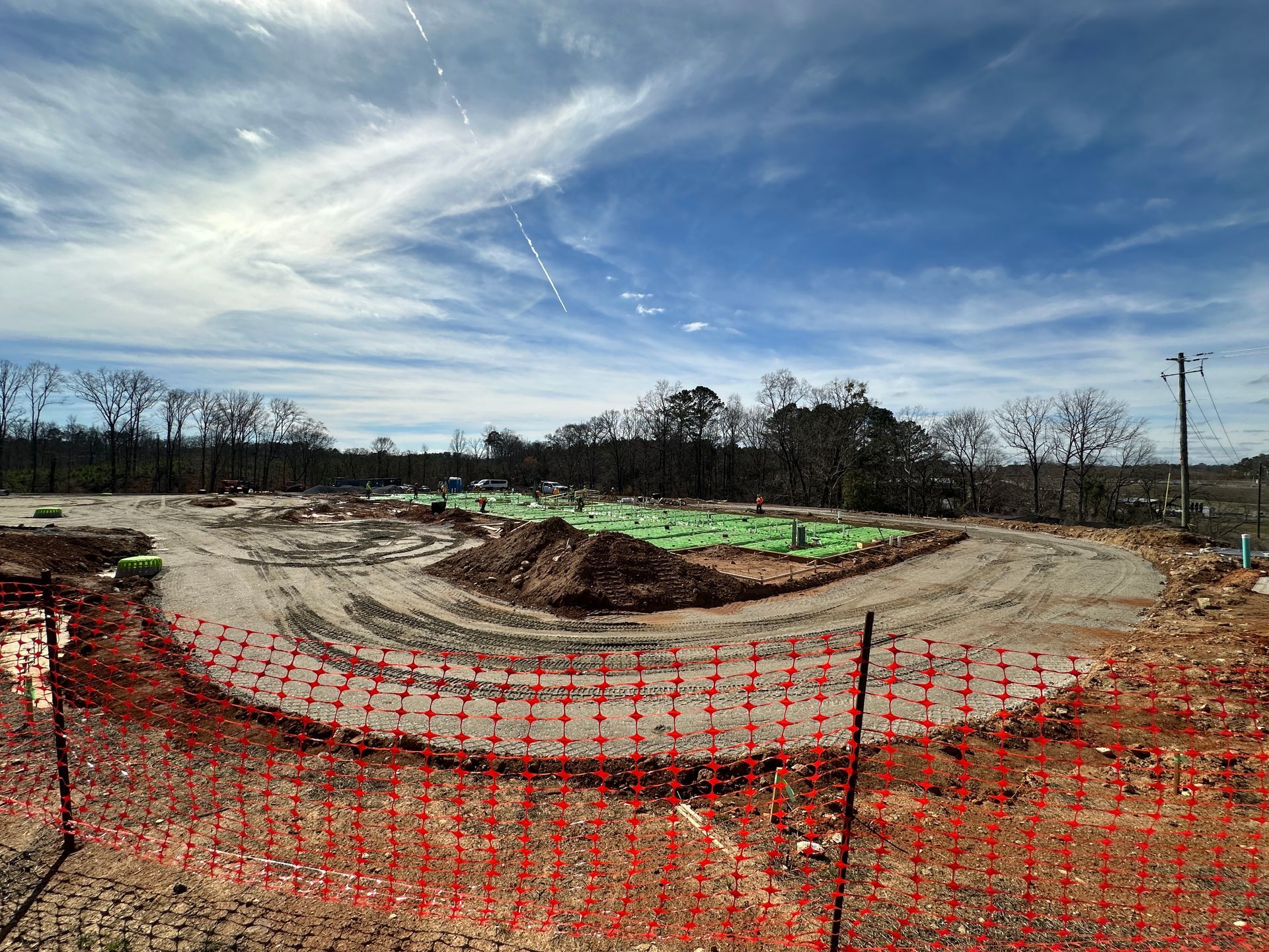 Construction site with red fencing, dirt, and green tarps under a blue sky.