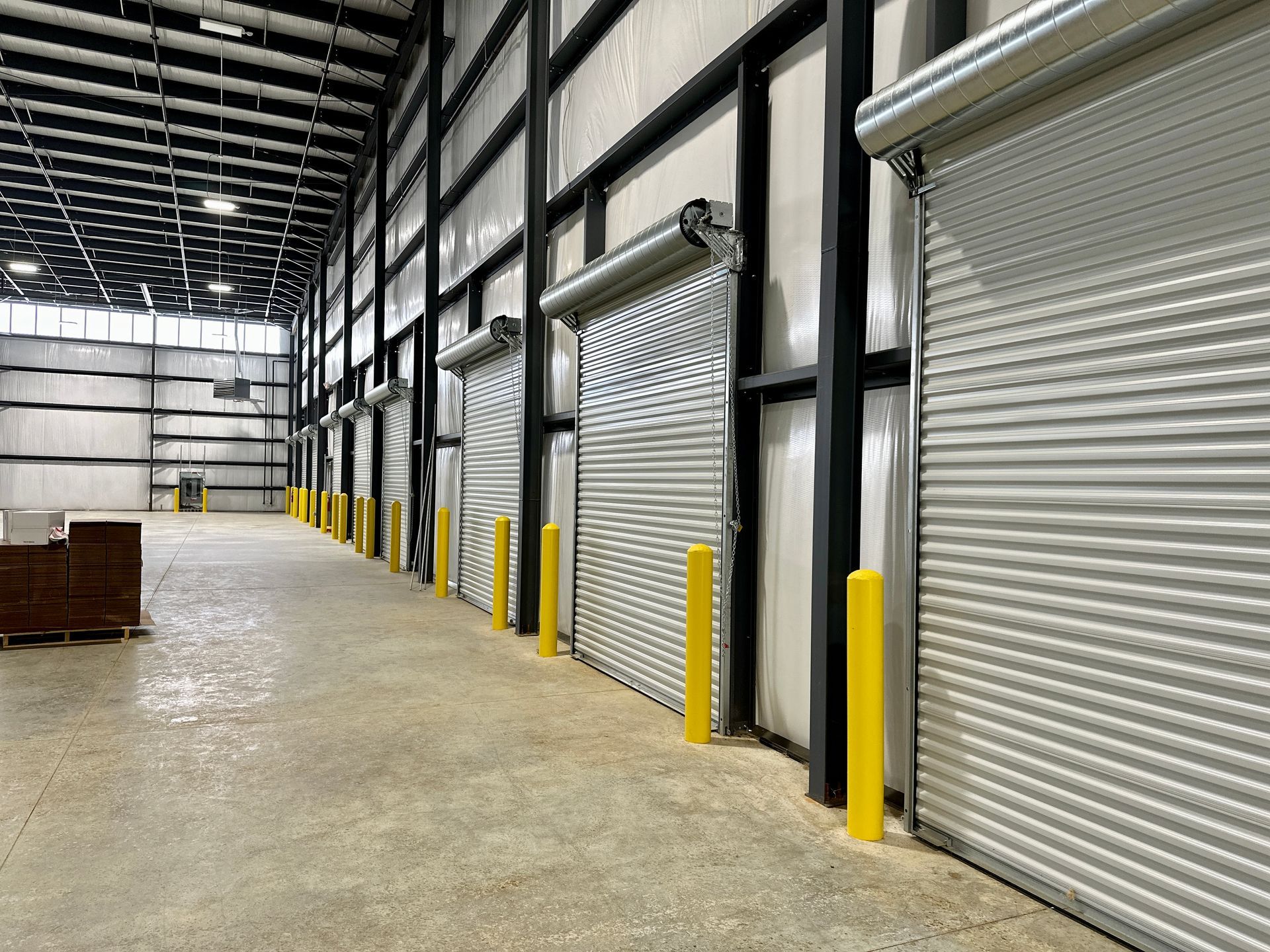 A large warehouse with a lot of roller shutters and yellow poles.