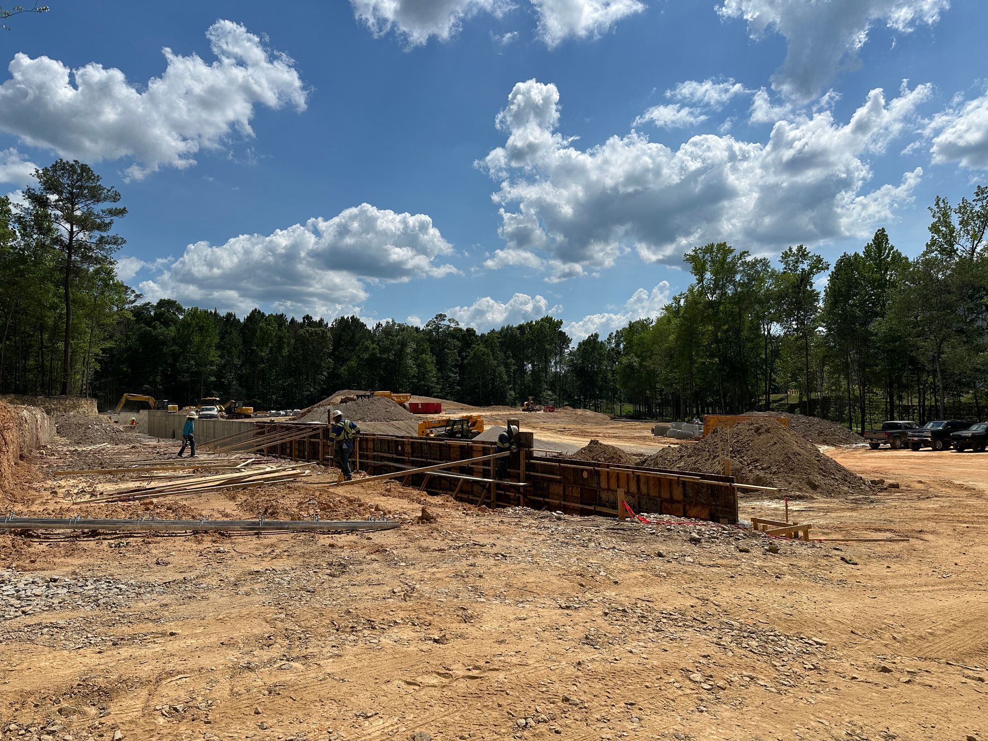 Cleared construction site with dirt piles and machinery under a blue sky with clouds