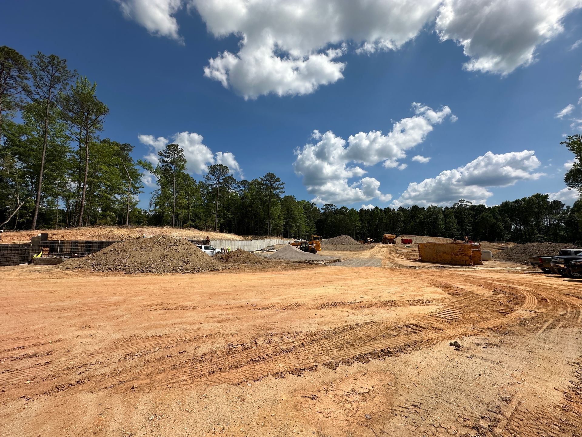 Construction site with cleared ground, earth piles, and a blue sky with scattered clouds