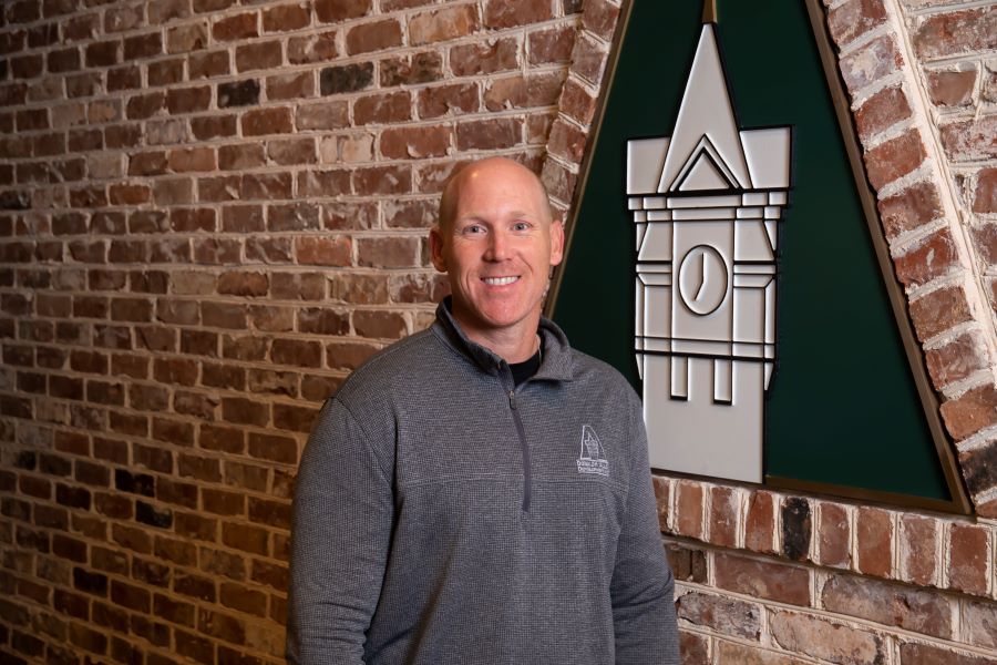A man is standing in front of a brick wall with a clock tower on it.