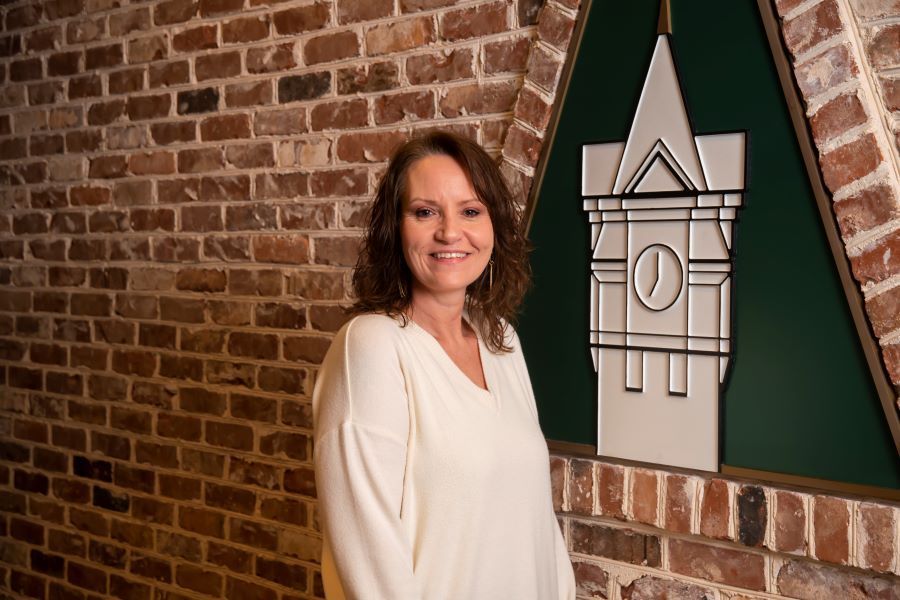 A woman is standing in front of a brick wall with a clock tower on it.