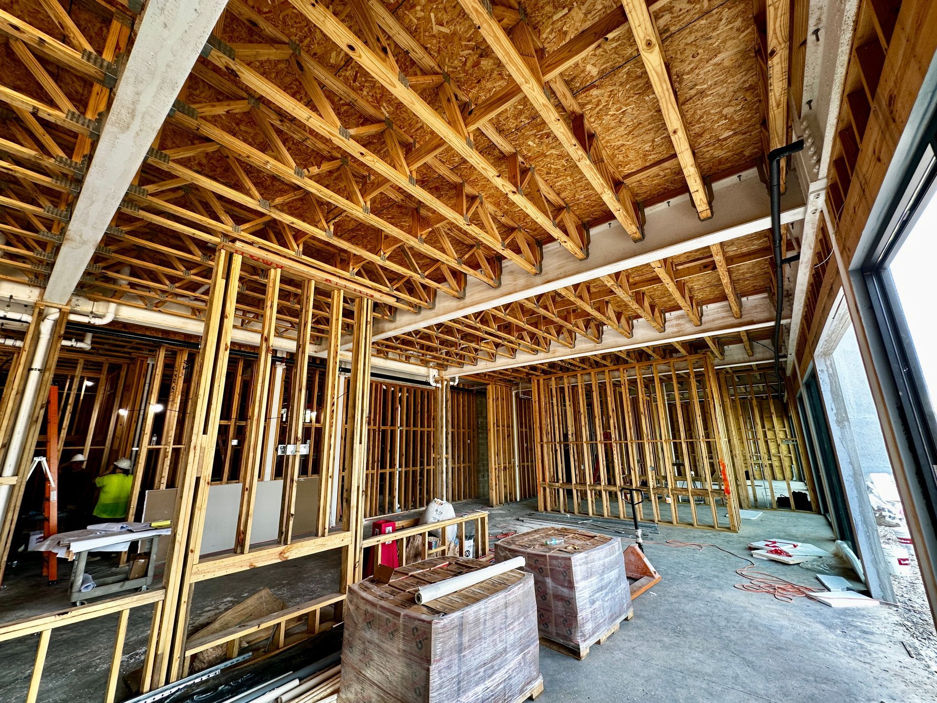 Interior of a house under construction with exposed wooden framing, plywood subfloor, and open window openings