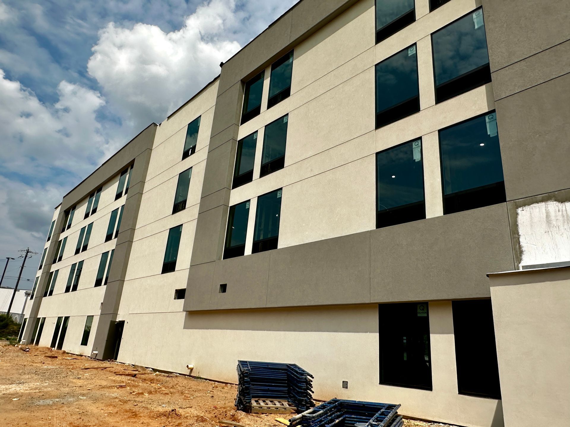 Modern apartment building exterior with beige and gray facade, large windows, and cloudy sky