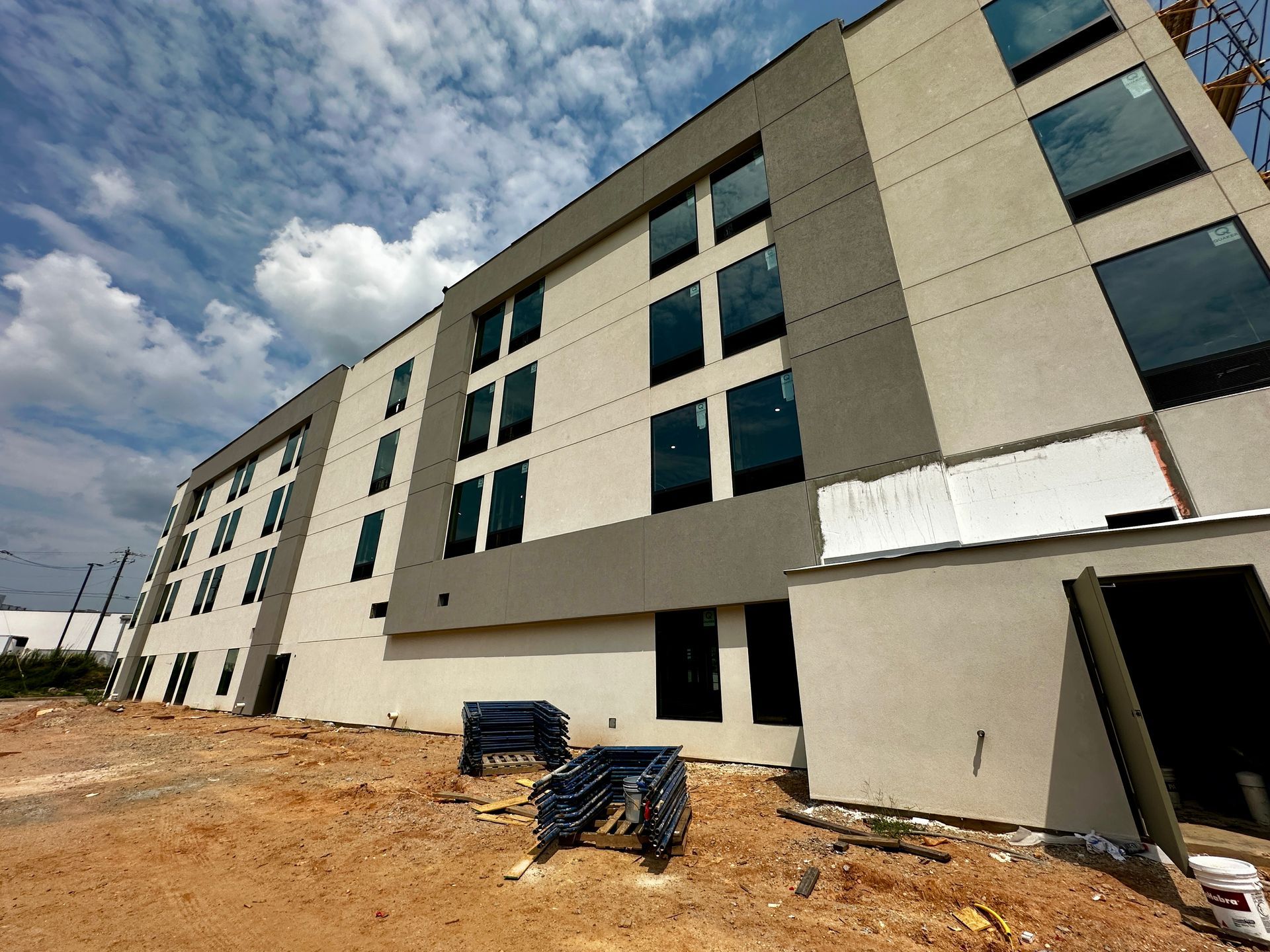 Modern multi-story building under construction with unfinished exterior and dirt foreground