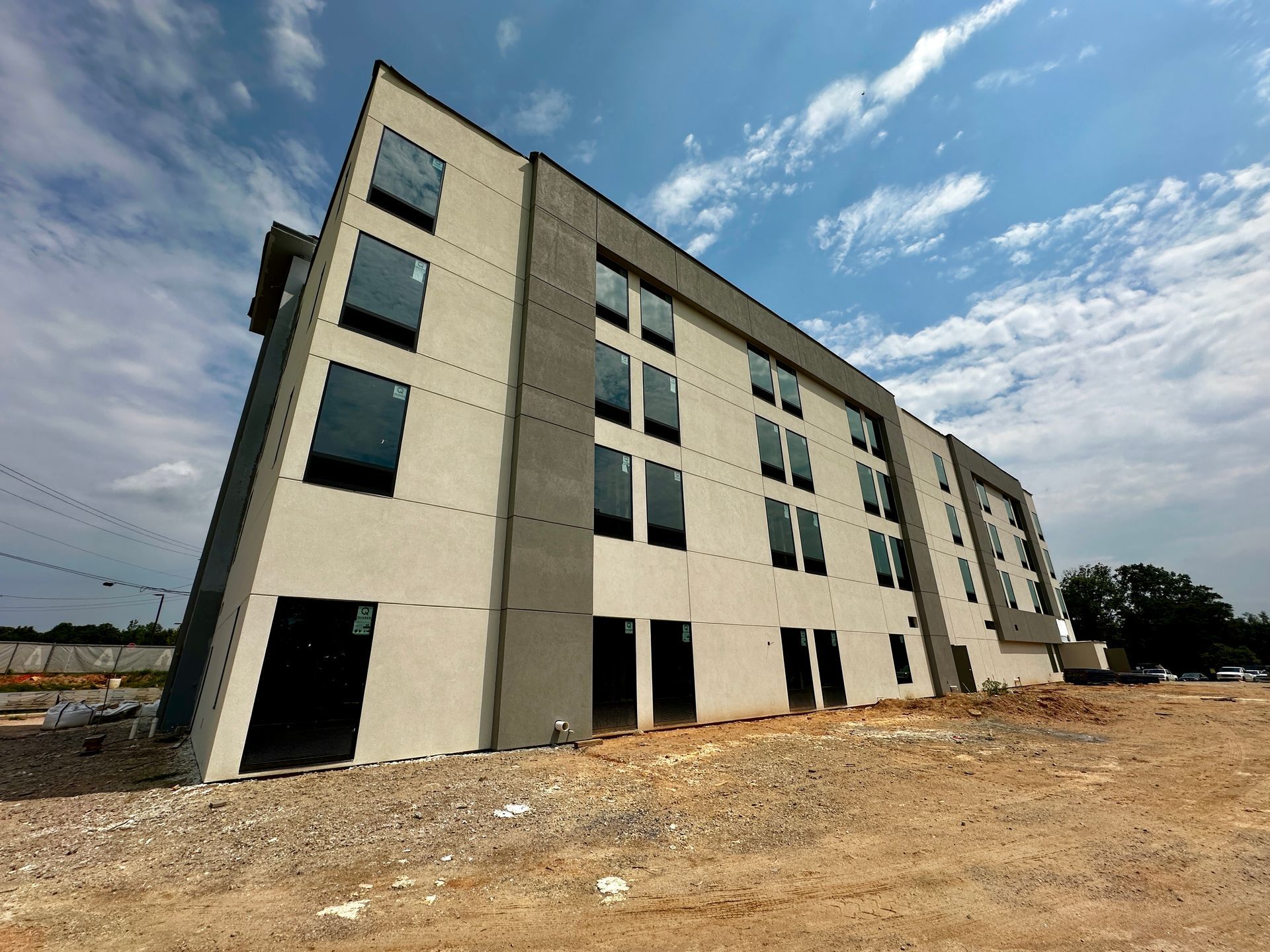 Three-story unfinished apartment building on a dirt lot under a partly cloudy sky