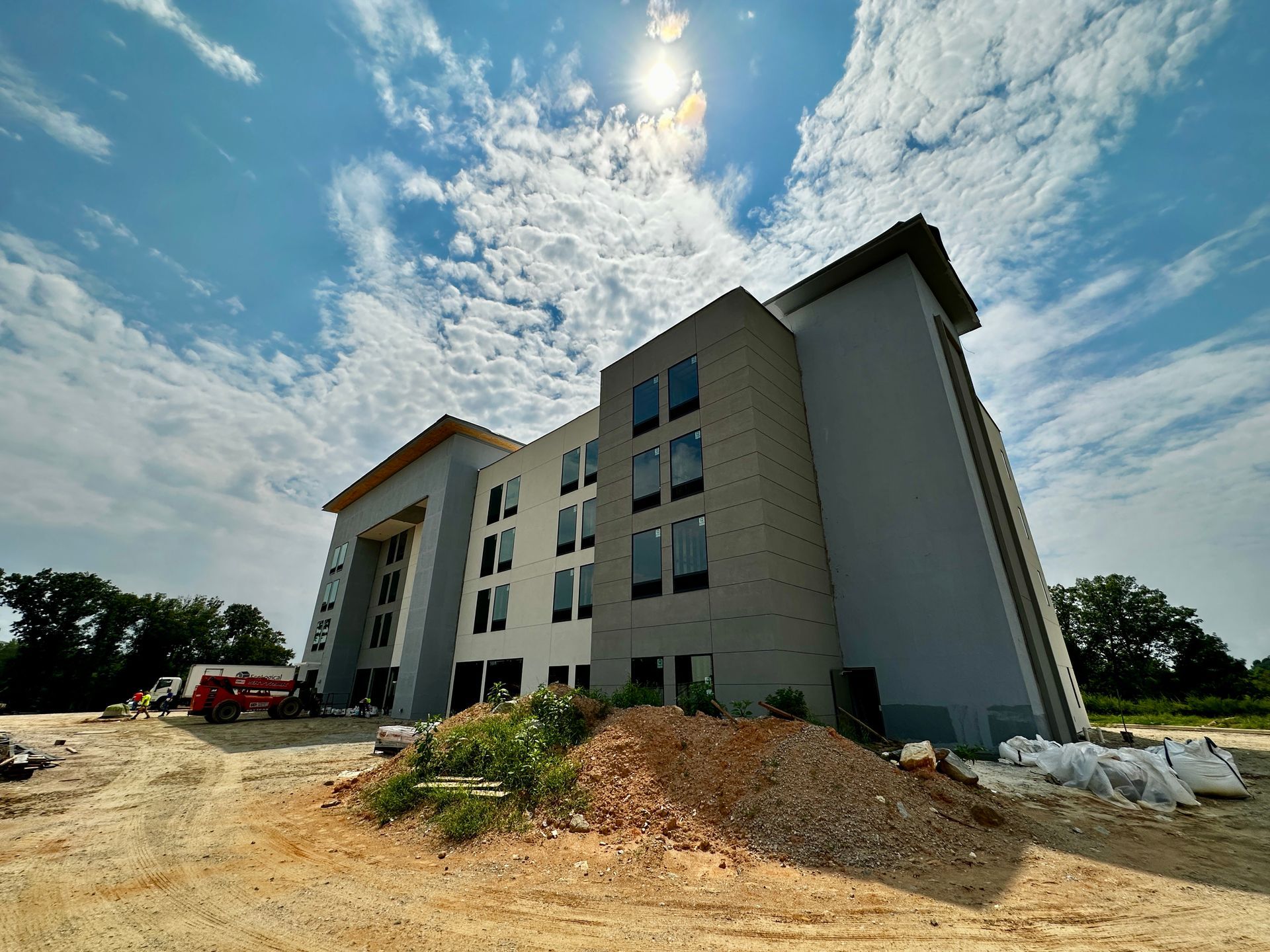 New gray apartment building under construction on a dirt lot under a bright sky