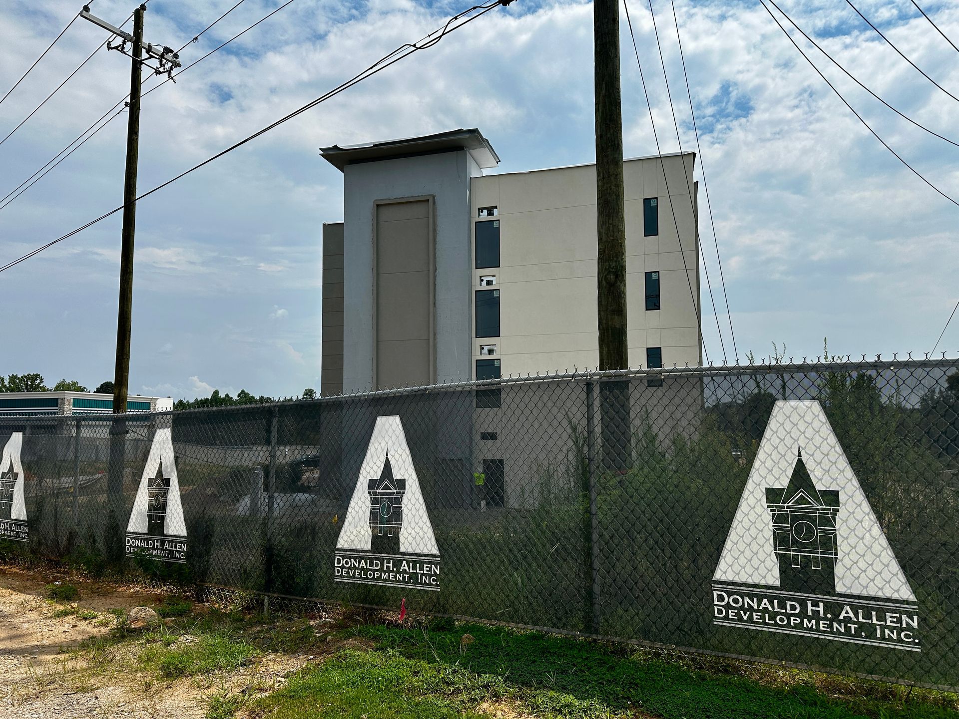 Concrete building behind chain-link fence with painted signs and utility poles under a cloudy sky