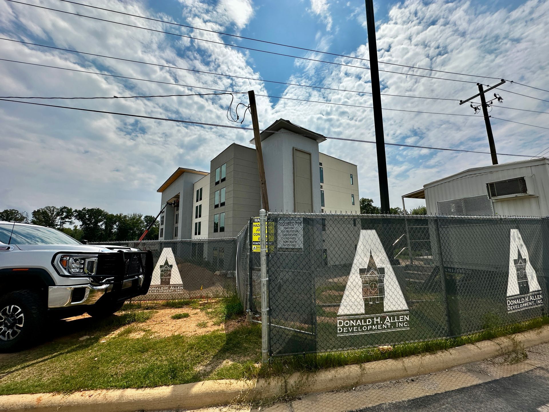 New apartment building behind a chain-link fence, with a parked truck and cloudy sky overhead