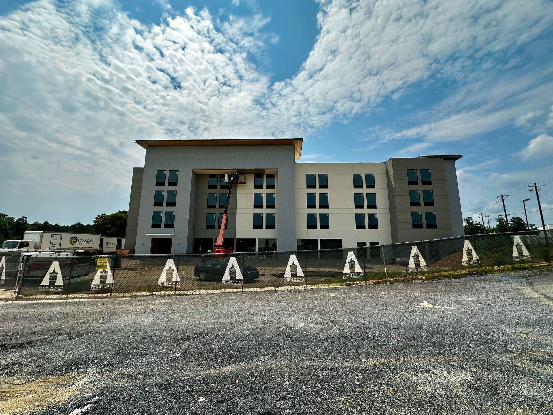 Modern white building with a red entry banner, stone frontage, and a cloudy blue sky above