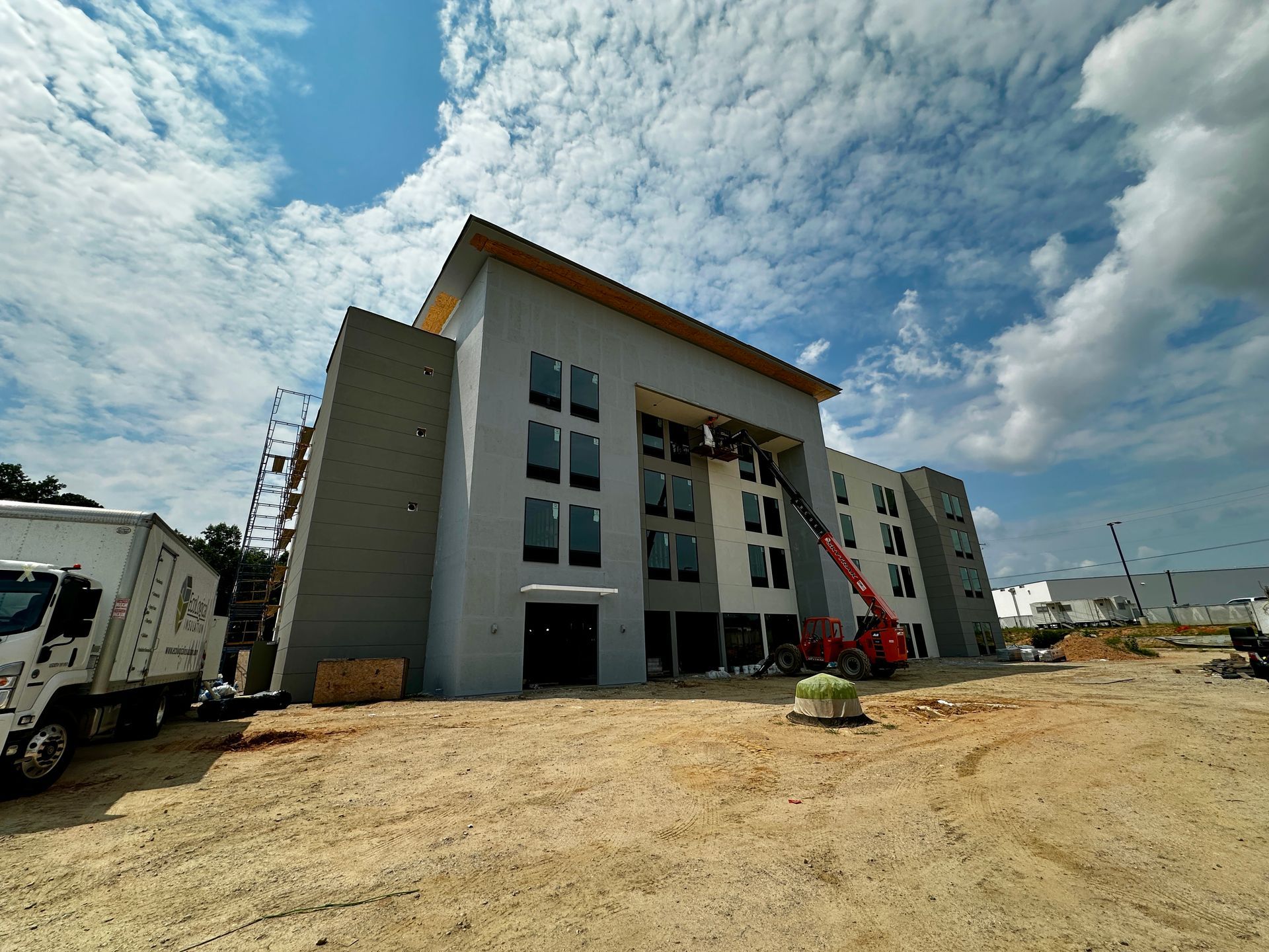 Modern multi-story building under construction with a crane, on a dirt lot beneath a cloudy sky
