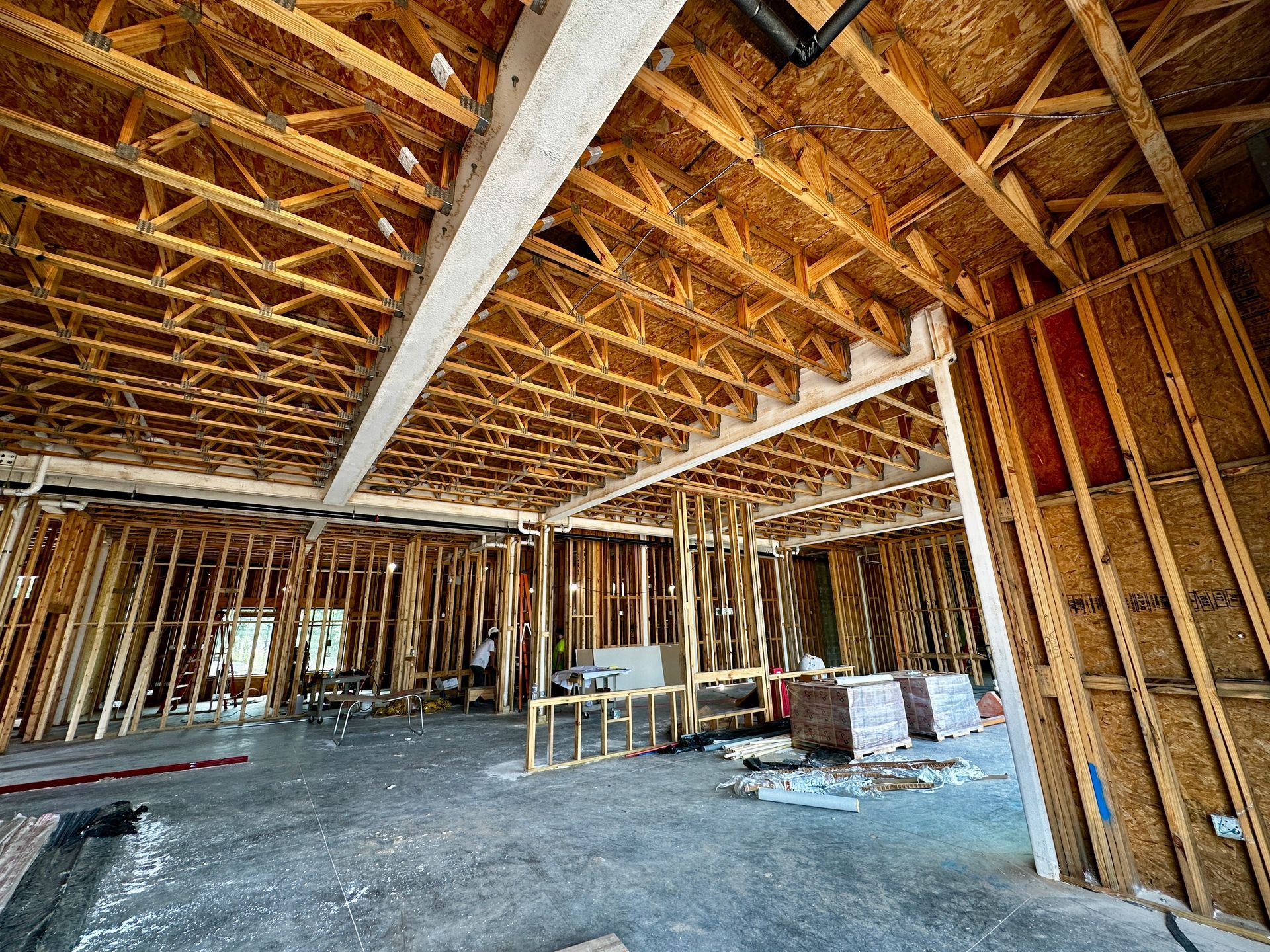 Partially framed house interior with exposed wooden trusses, studs, and construction materials on the floor