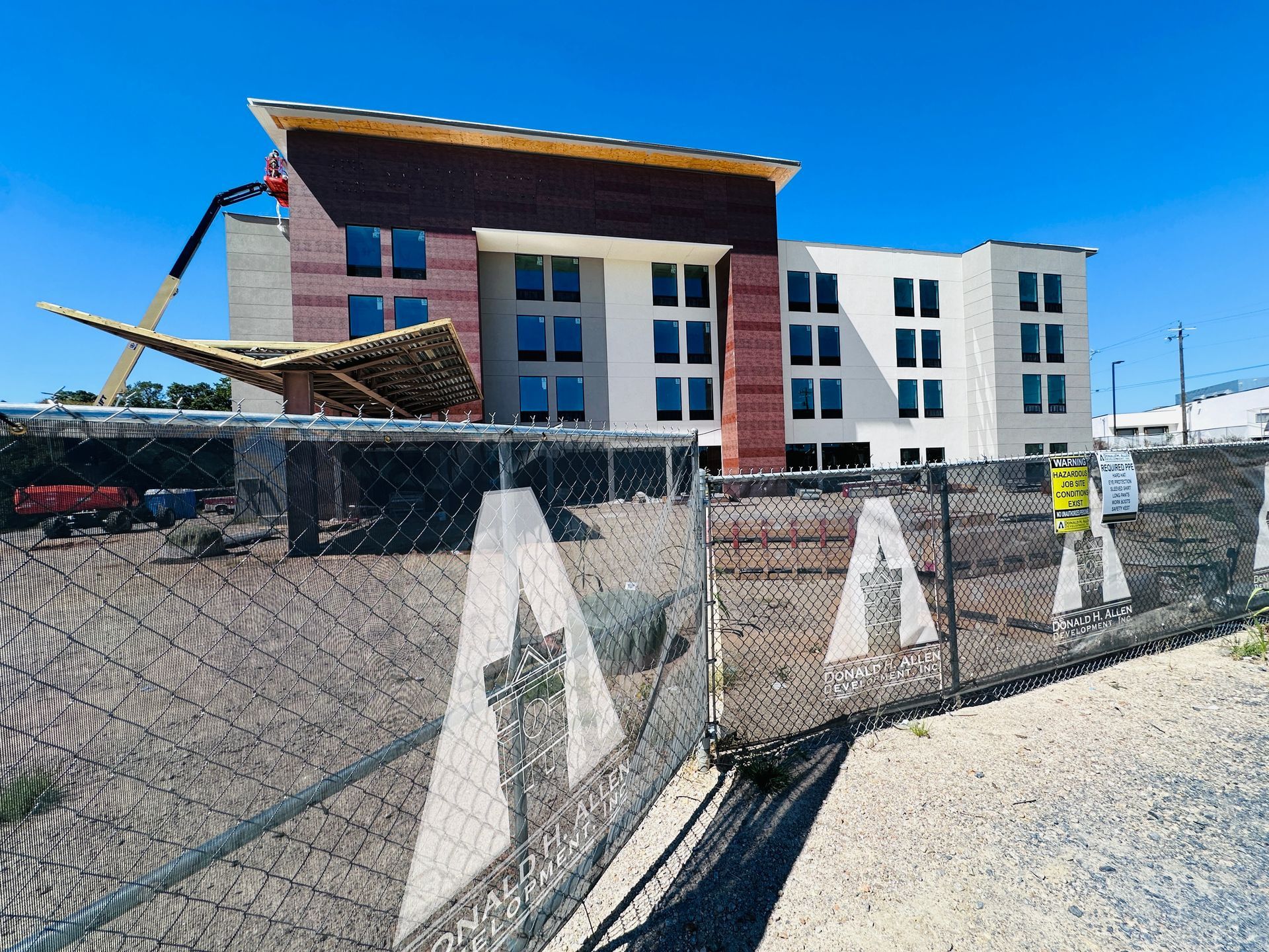 Construction site with hotel building behind chain-link fence under a bright blue sky