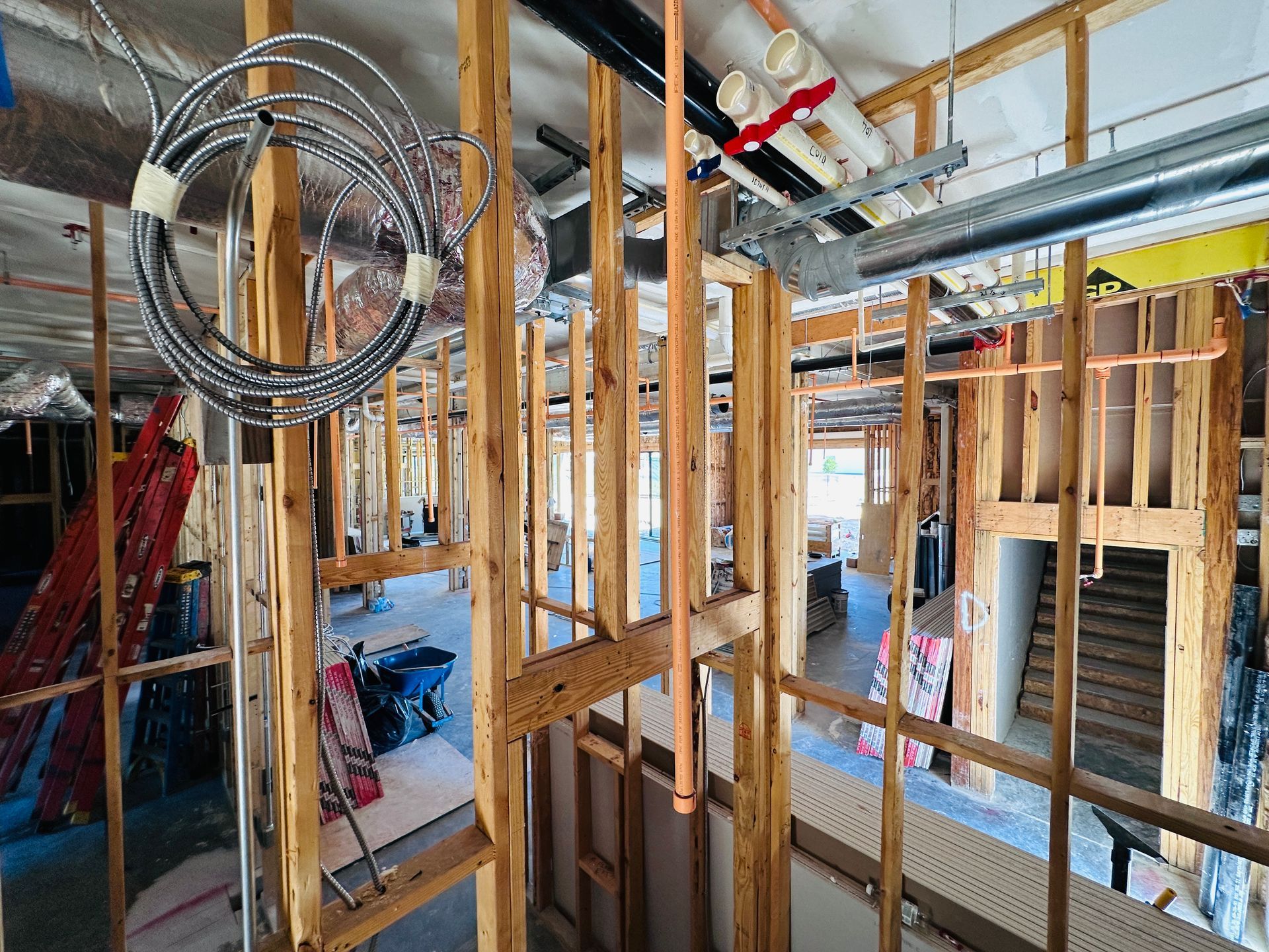 Interior construction site with exposed wood framing, hanging wires, and ceiling ductwork under installation