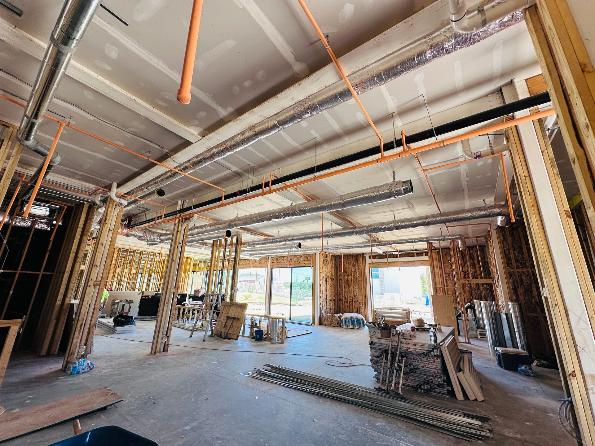 Unfinished hotel interior with exposed ceiling beams, ducts, and construction materials on the floor.
