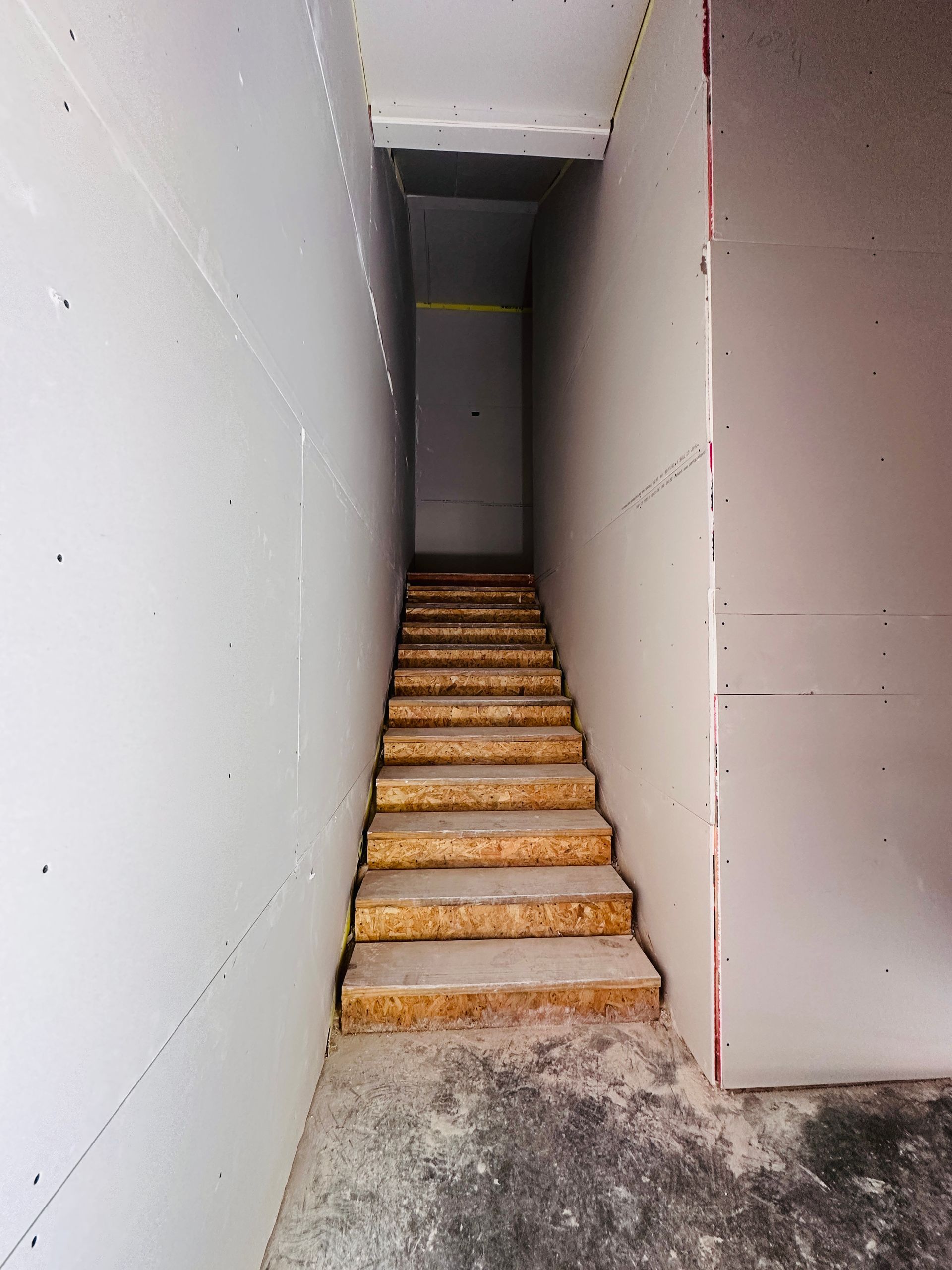 Narrow unfinished stairwell with wooden steps leading upward between white walls