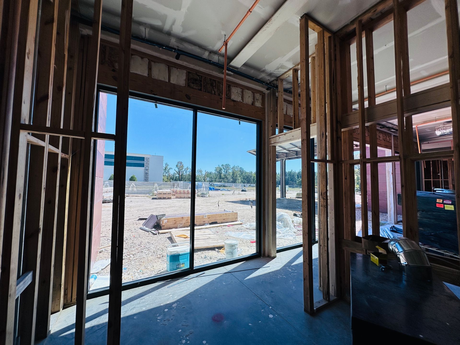 Interior construction site with open framing and a large doorway looking out to a bright outdoor lot.