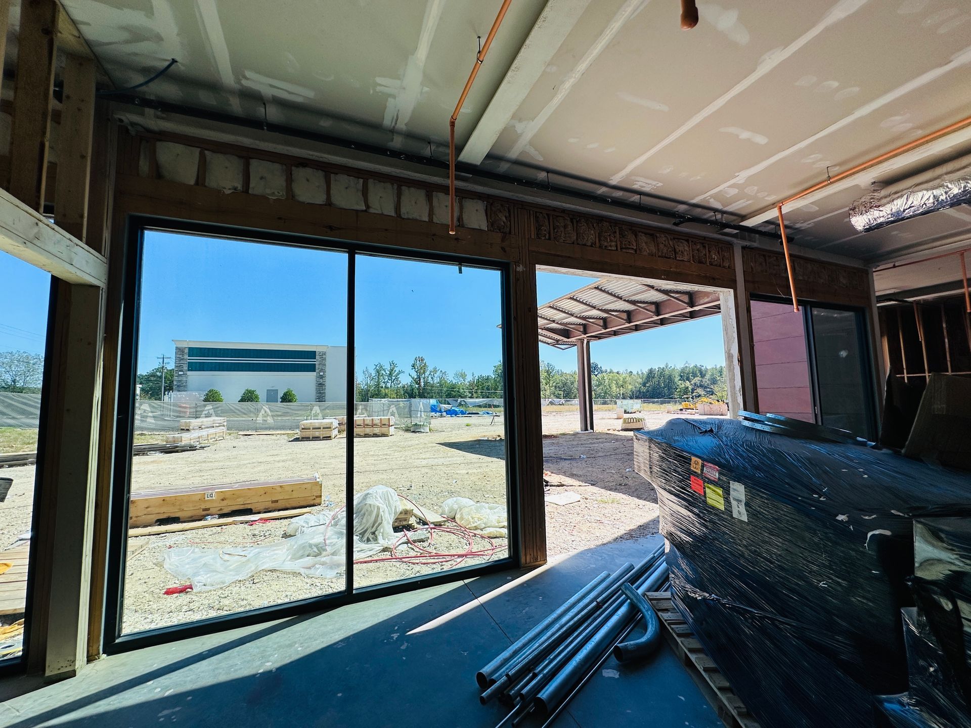 Interior construction site with large sliding glass doors opening to a sandy outdoor area and blue sky.