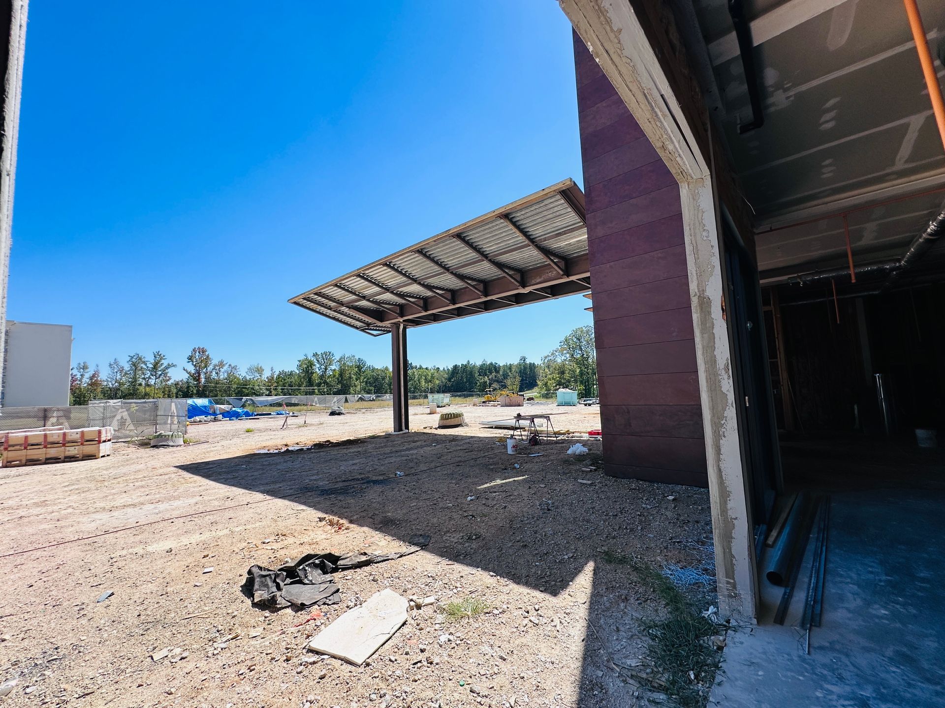 Open yard with a covered brick structure casting shade over dirt ground under a bright blue sky