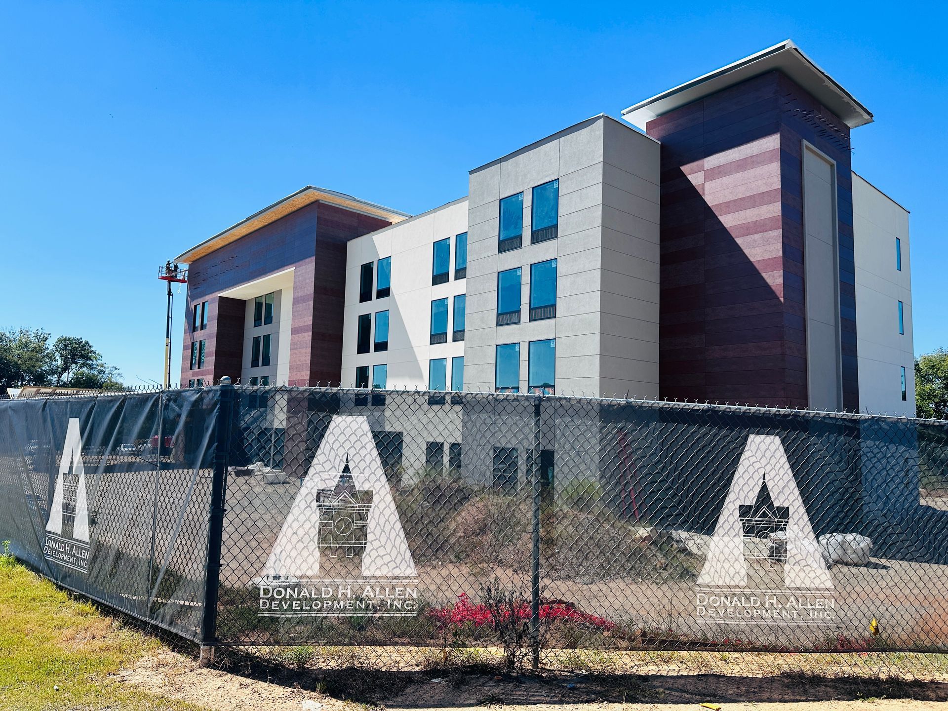 Modern hotel building behind a chain-link fence under a clear blue sky.
