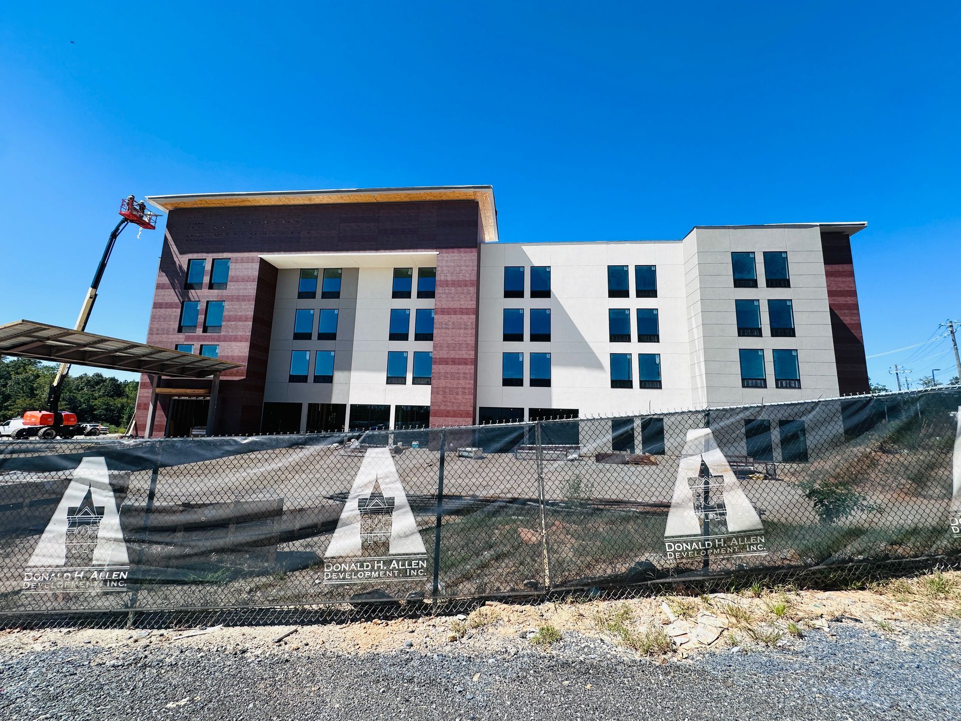 Modern three-story building with white and brick exterior behind a chain-link fence under a blue sky