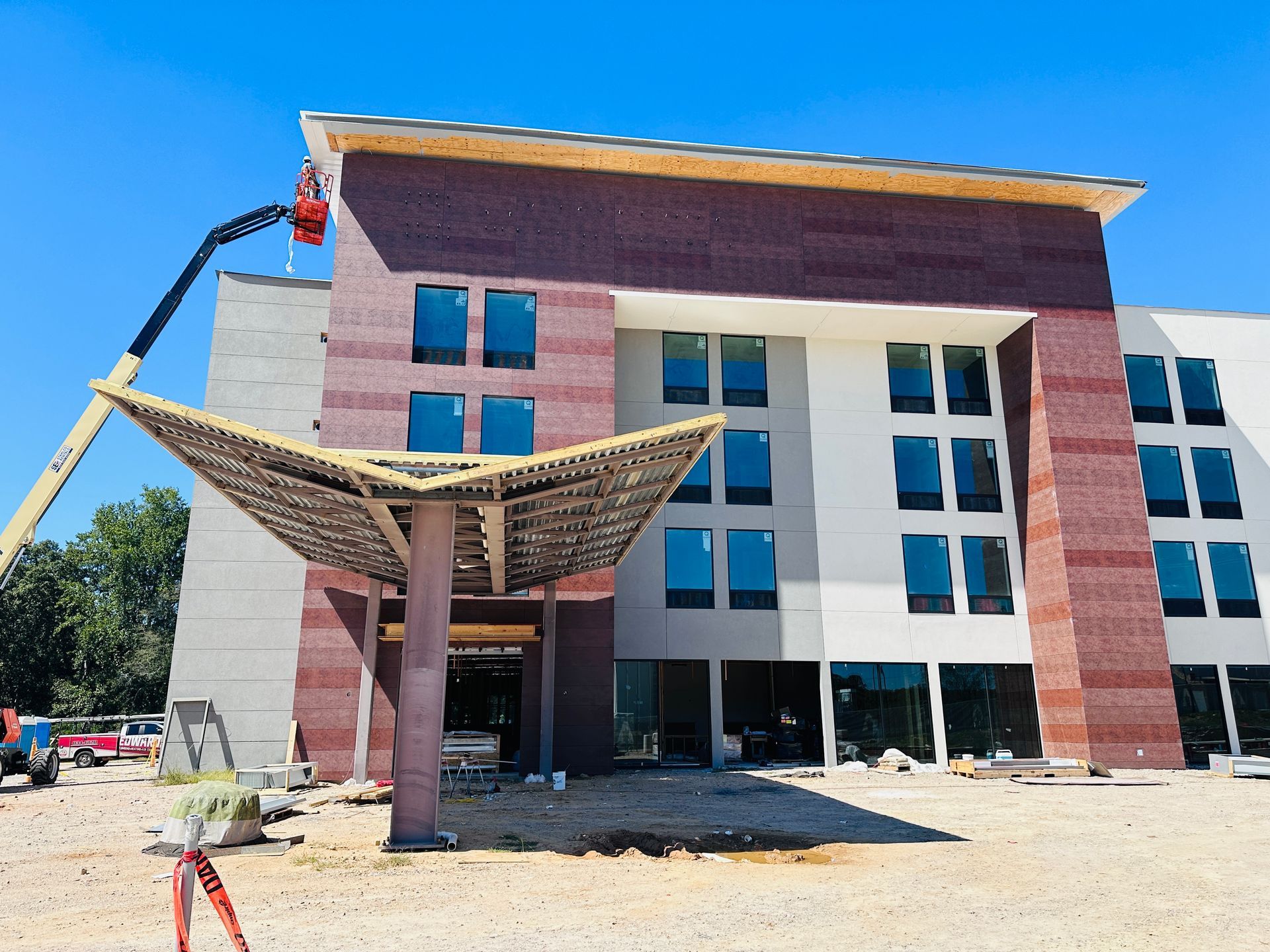 Modern building facade with red brick, white columns, and a shaded entrance canopy under a blue sky