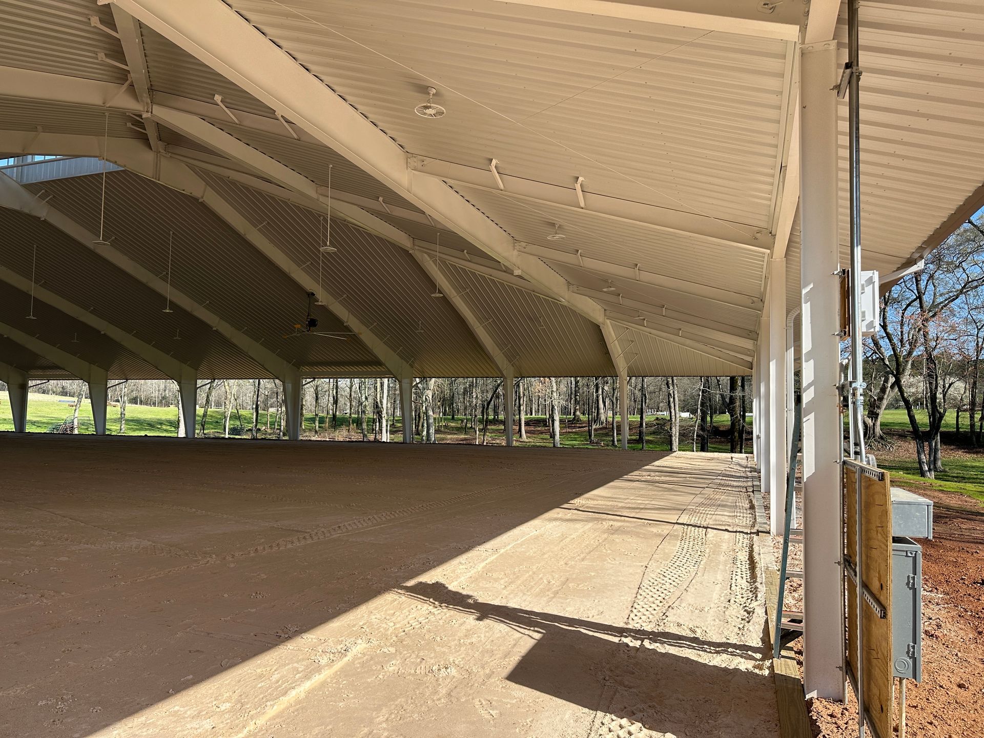 Open-air metal pavilion with a peaked roof, supported by white columns, overlooking a field with trees.