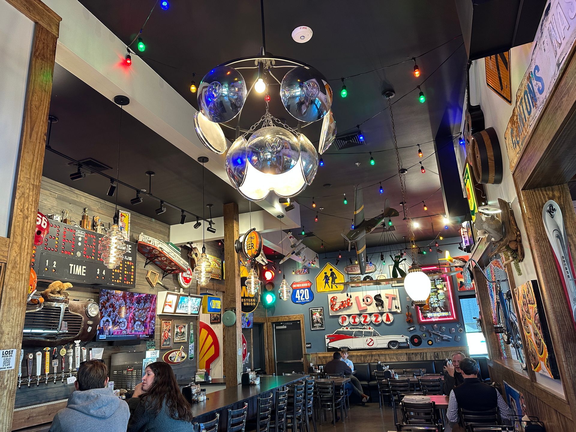 Restaurant interior with black ceiling, disco ball, and eclectic wall decor. People seated at bar and tables.